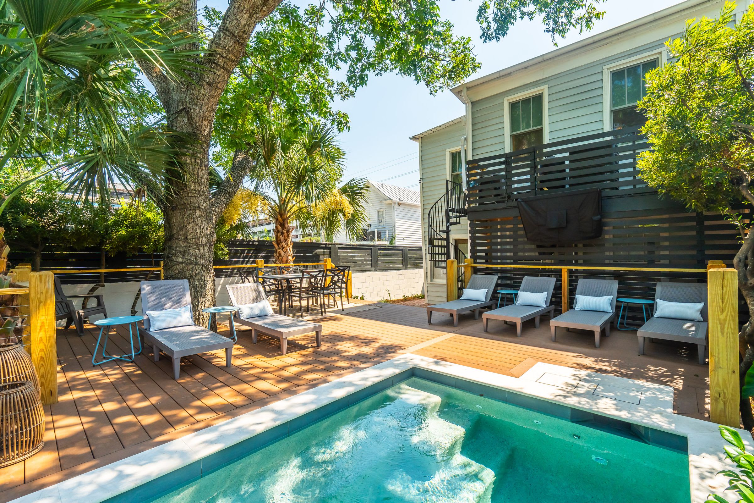 A small pool with a deck and lounge chairs surrounded by trees and a building