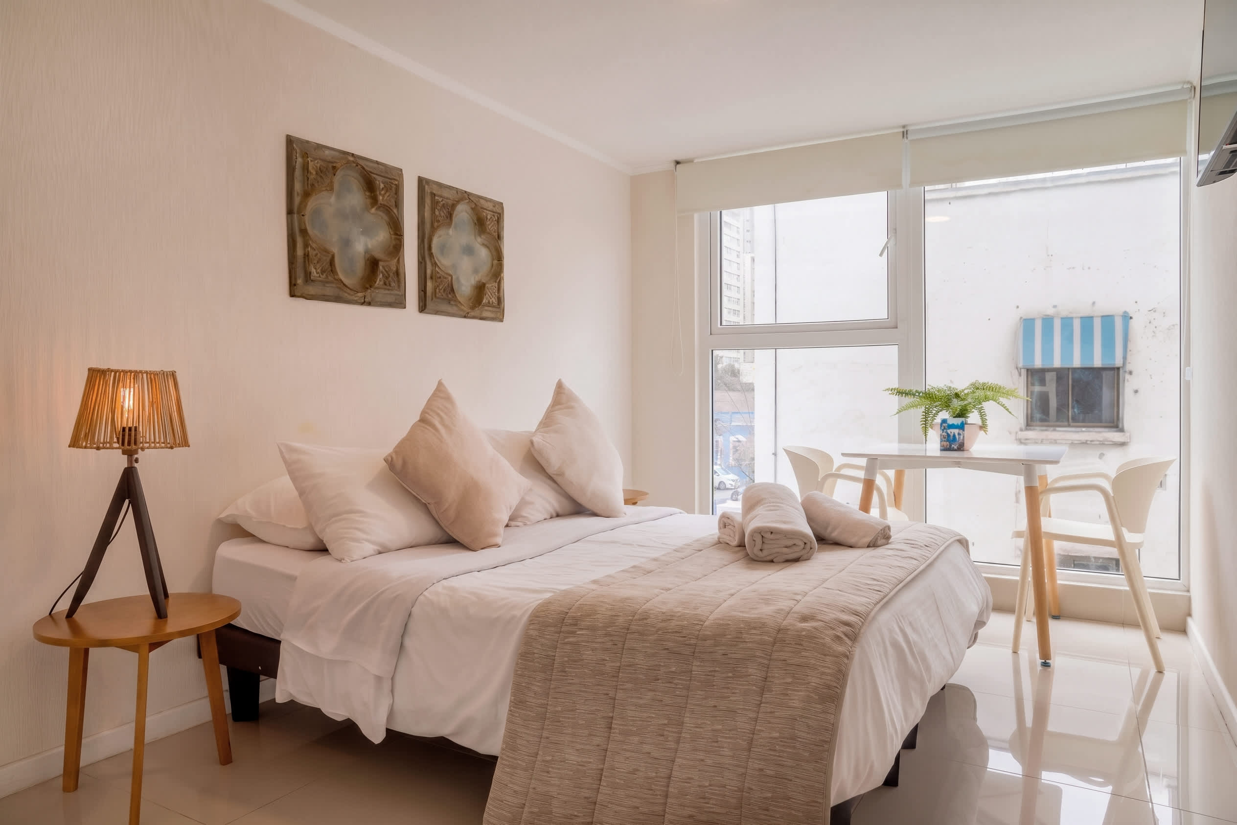 Bright and cozy studio with a comfortable bed and dining area by a large window, perfect for a relaxing stay.