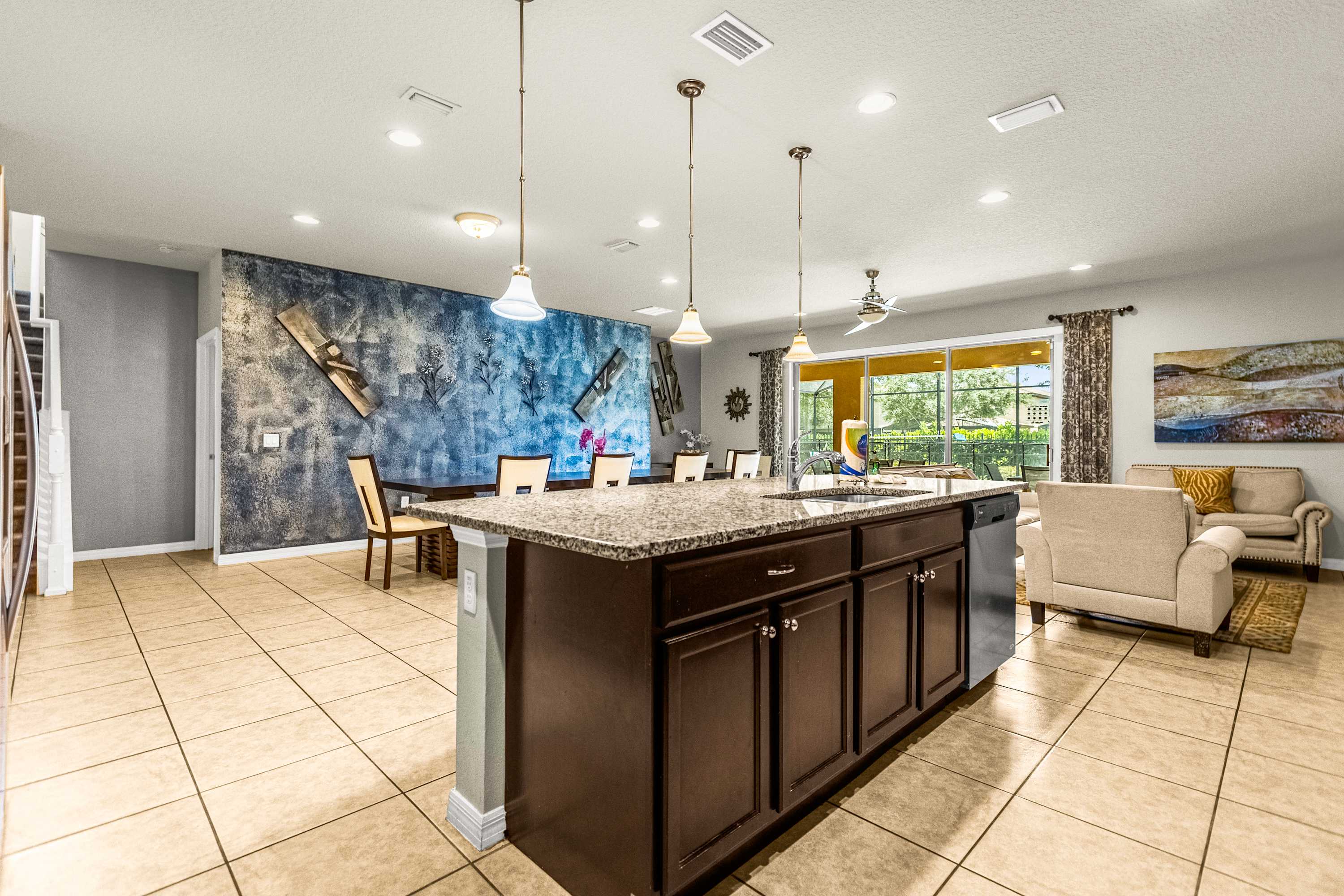 Open-plan kitchen with a granite island, spacious dining table, and sliding doors opening to a lush outdoor setting.