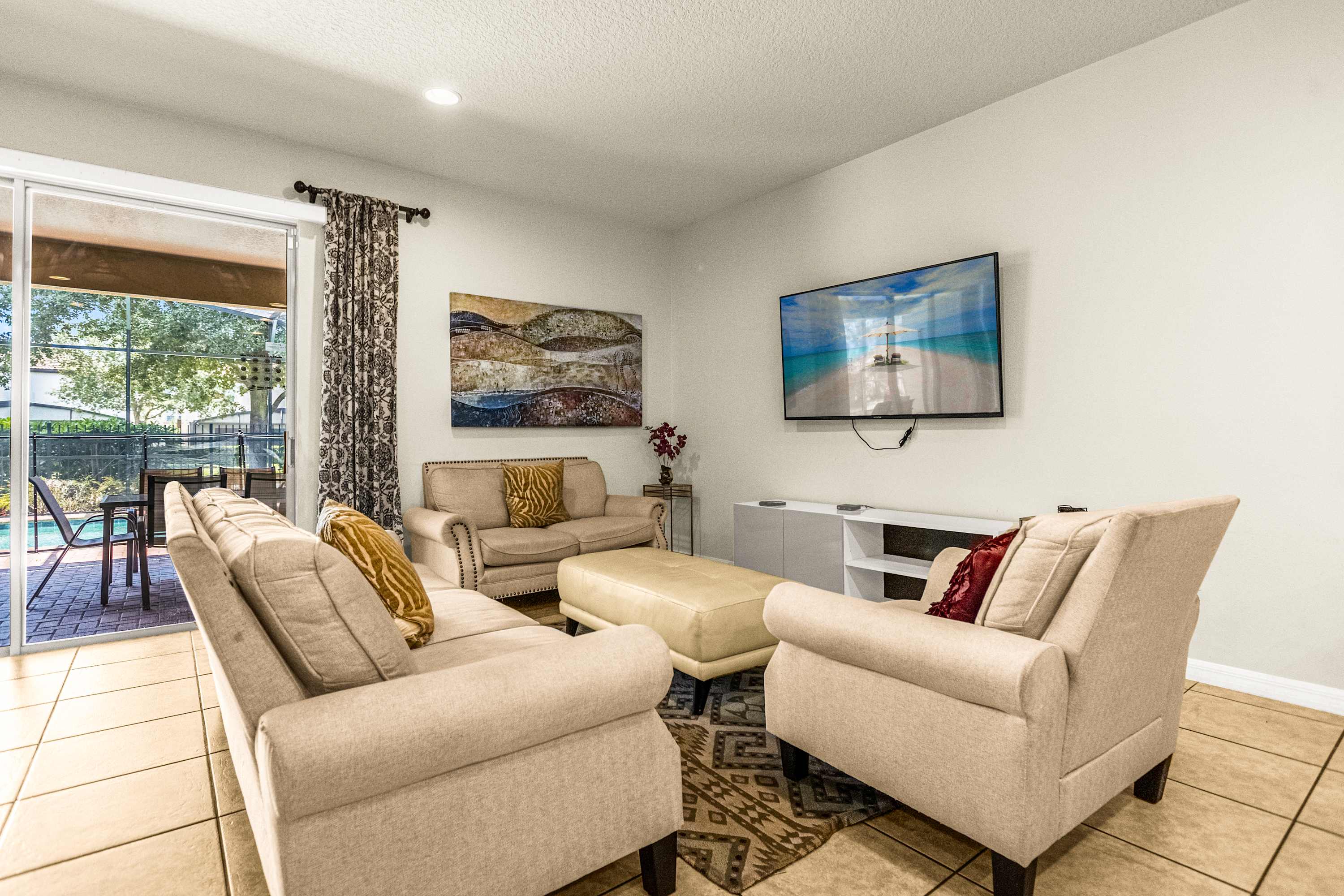 Private living room with plush cream seating, a large TV, and sliding doors opening to the poolside patio.