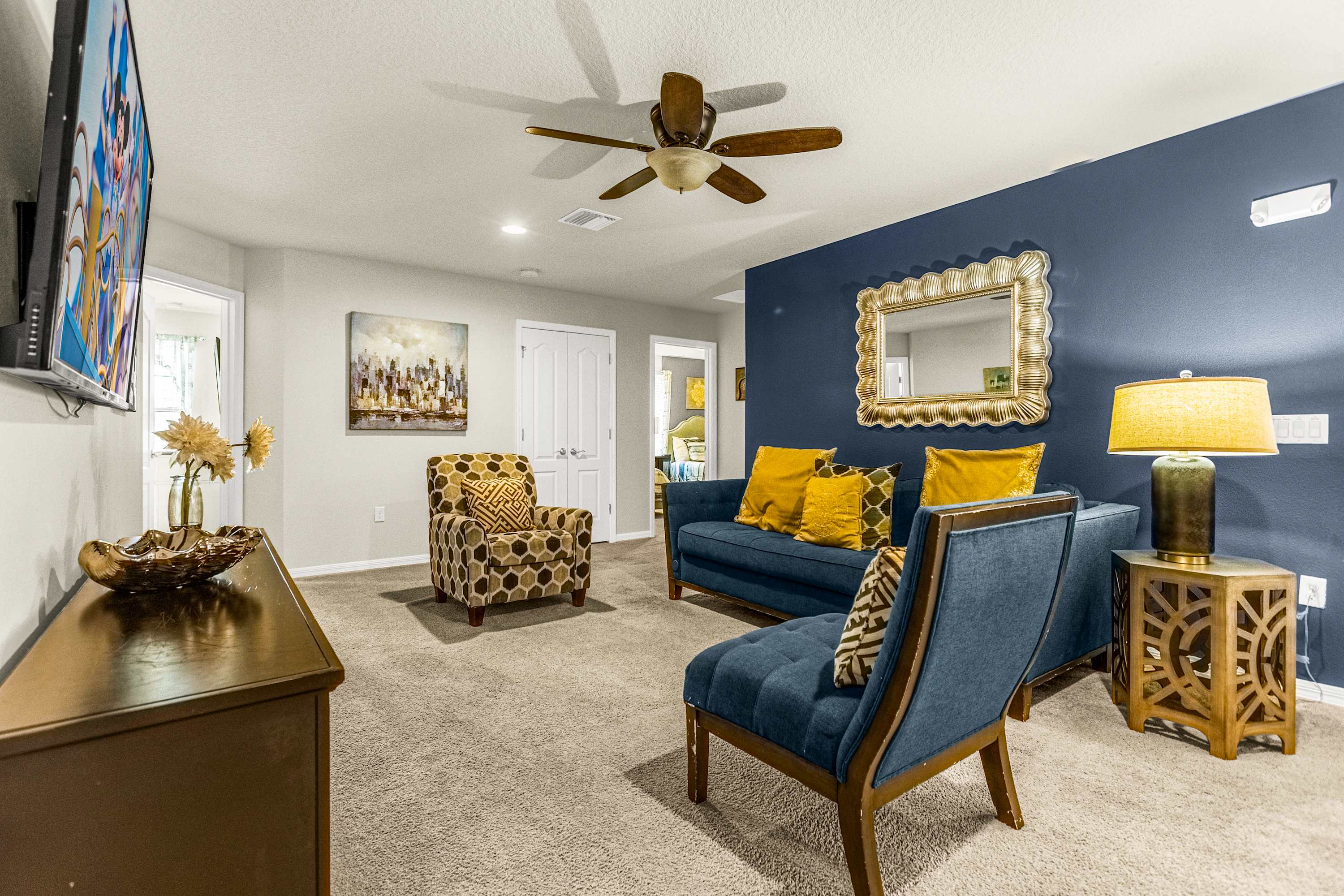 Relax in the stylish living room with plush navy seating, gold accent pillows, and a large TV for group entertainment.