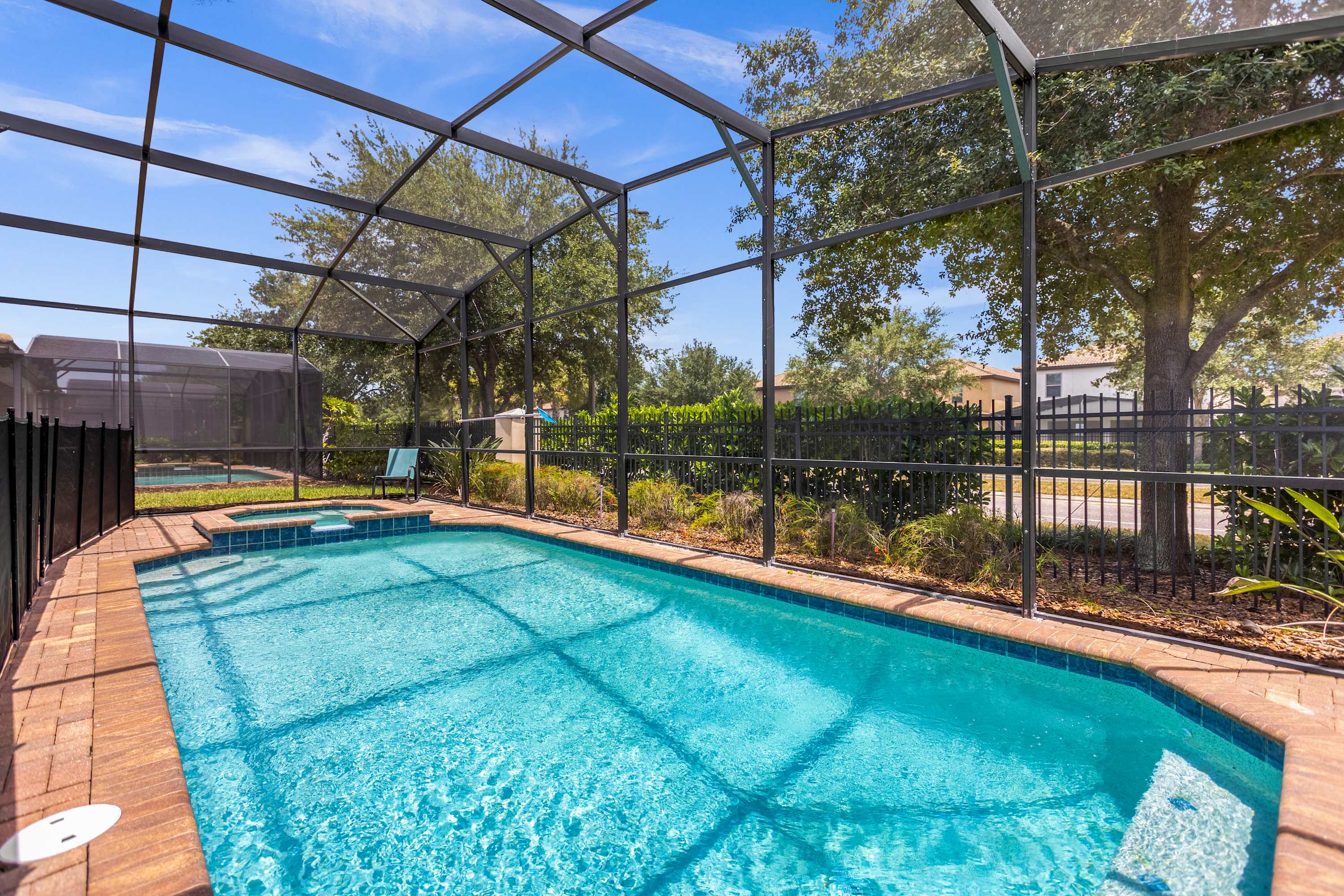 Private screened pool with a raised tiled spa, turquoise water, sunny paver deck, and mature trees creating a relaxing outdoor retreat.