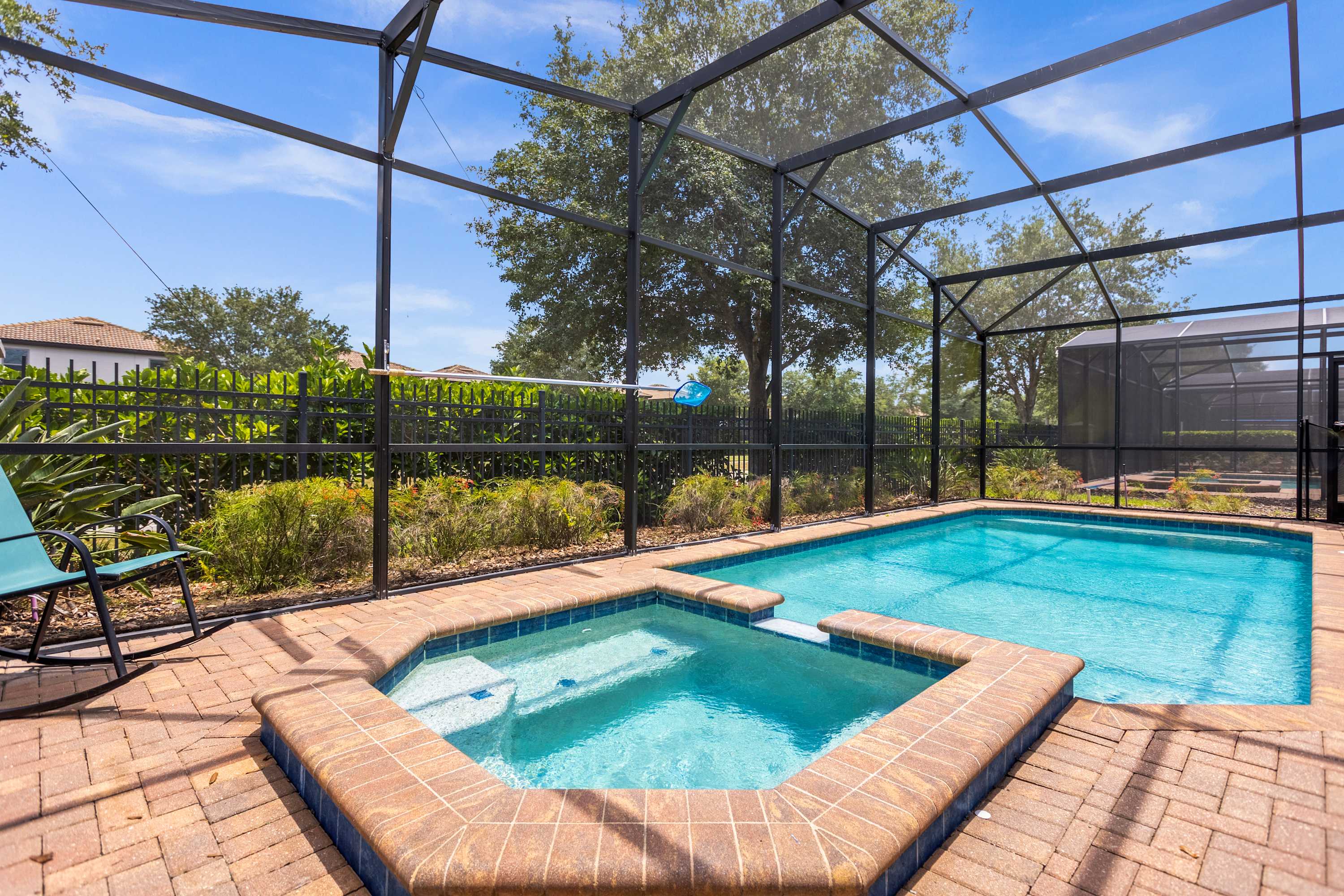 Private screened pool and bubbling hot tub surrounded by lush greenery, with a sunny brick-paved deck for relaxing outdoors.