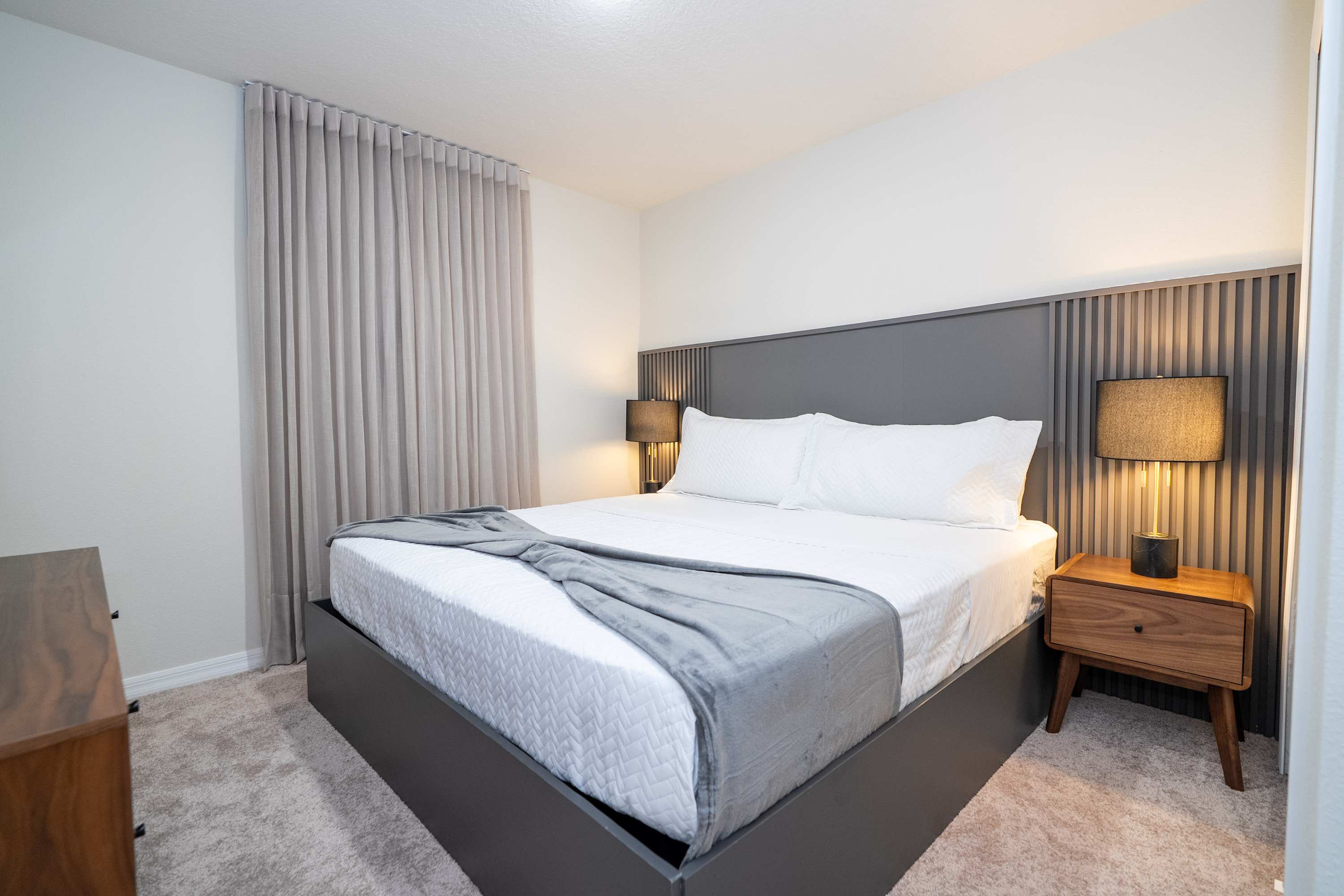 A peaceful king bedroom setup framed by soft bedside lamps and elegant, floor-to-ceiling window curtains