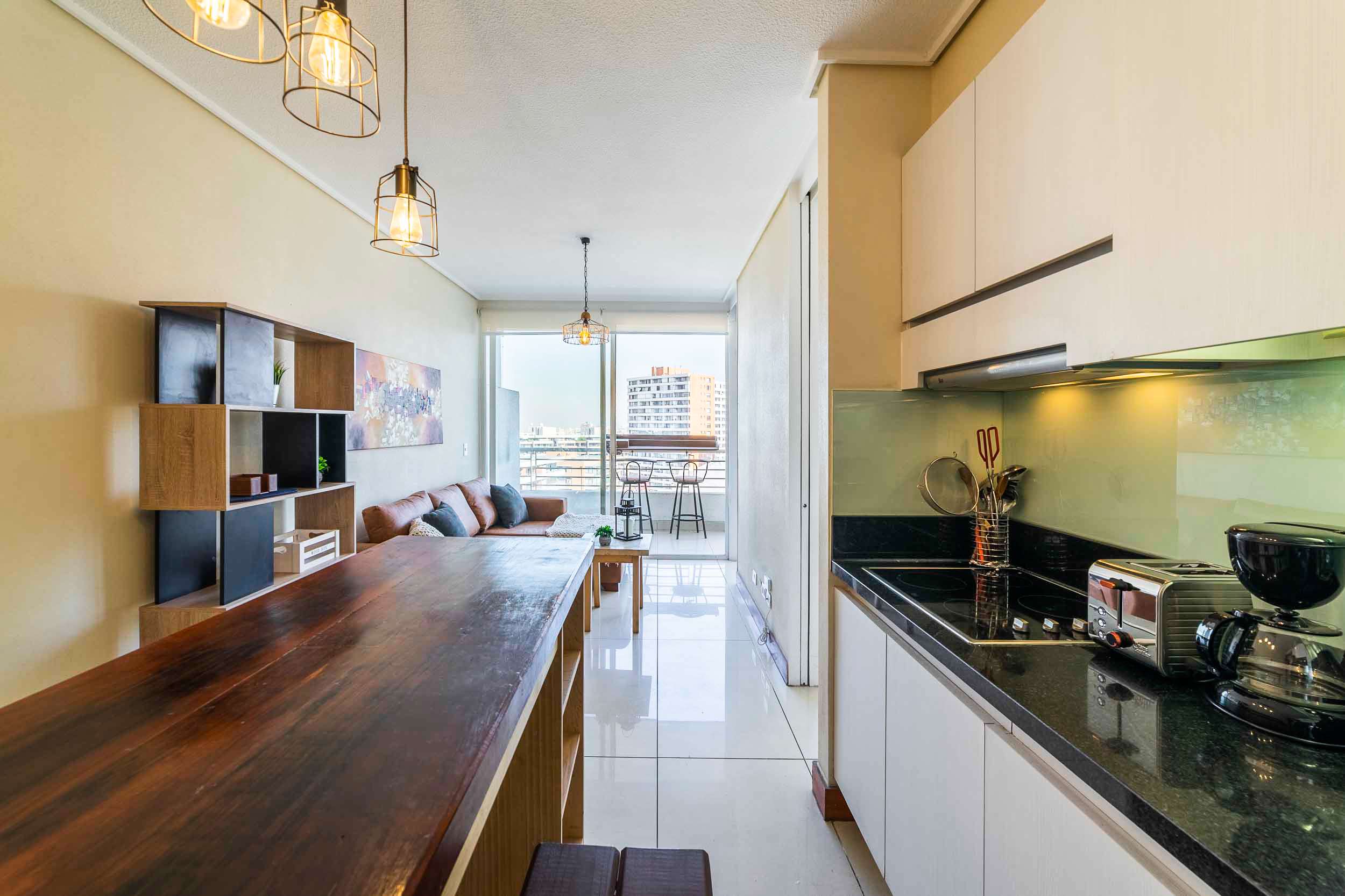 Modern studio kitchen with a wood dining table, complete appliances, and a bright balcony overlooking the city.