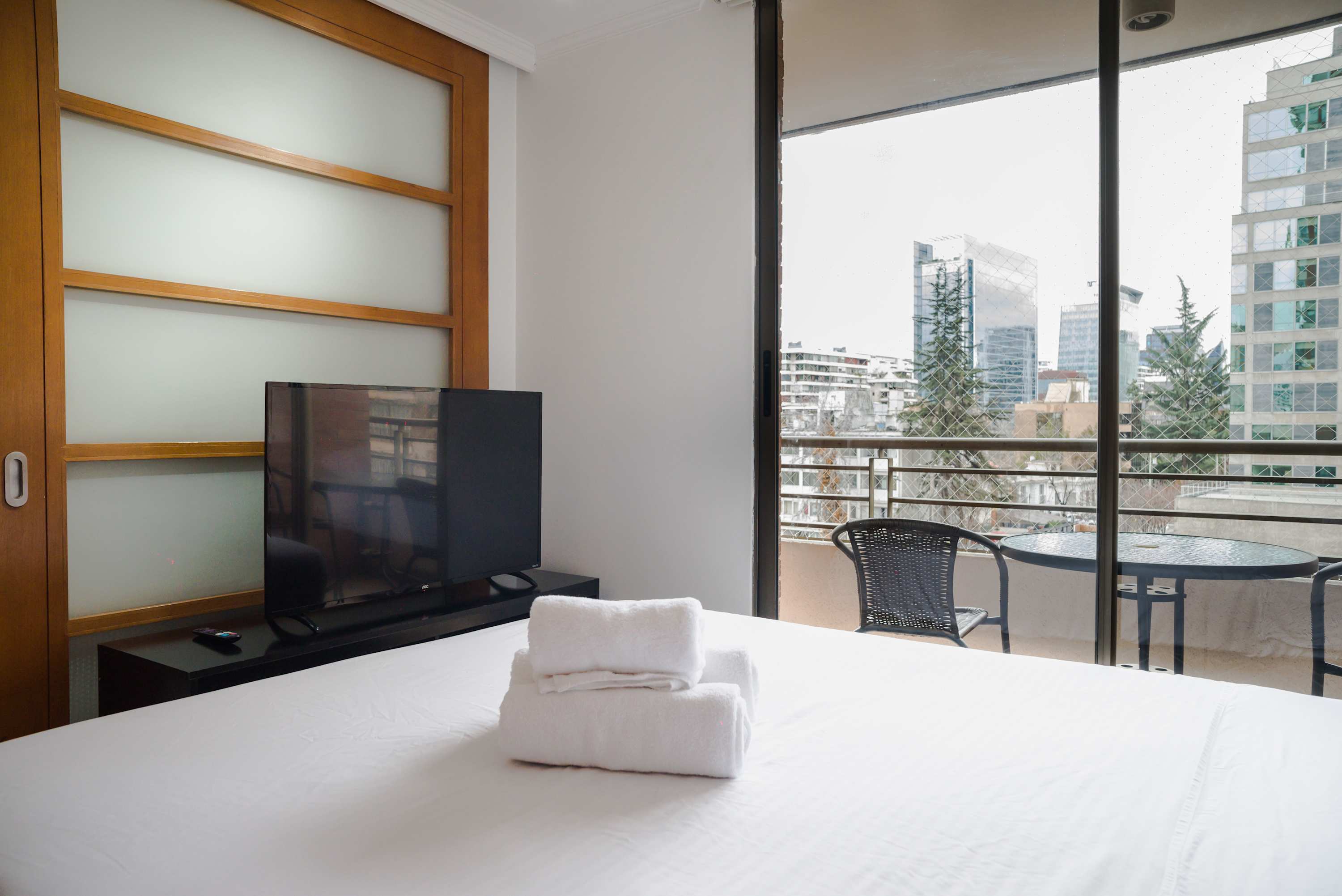 Relax in a cozy bedroom with a balcony offering stunning city views, perfect for unwinding after a day of exploring Santiago.