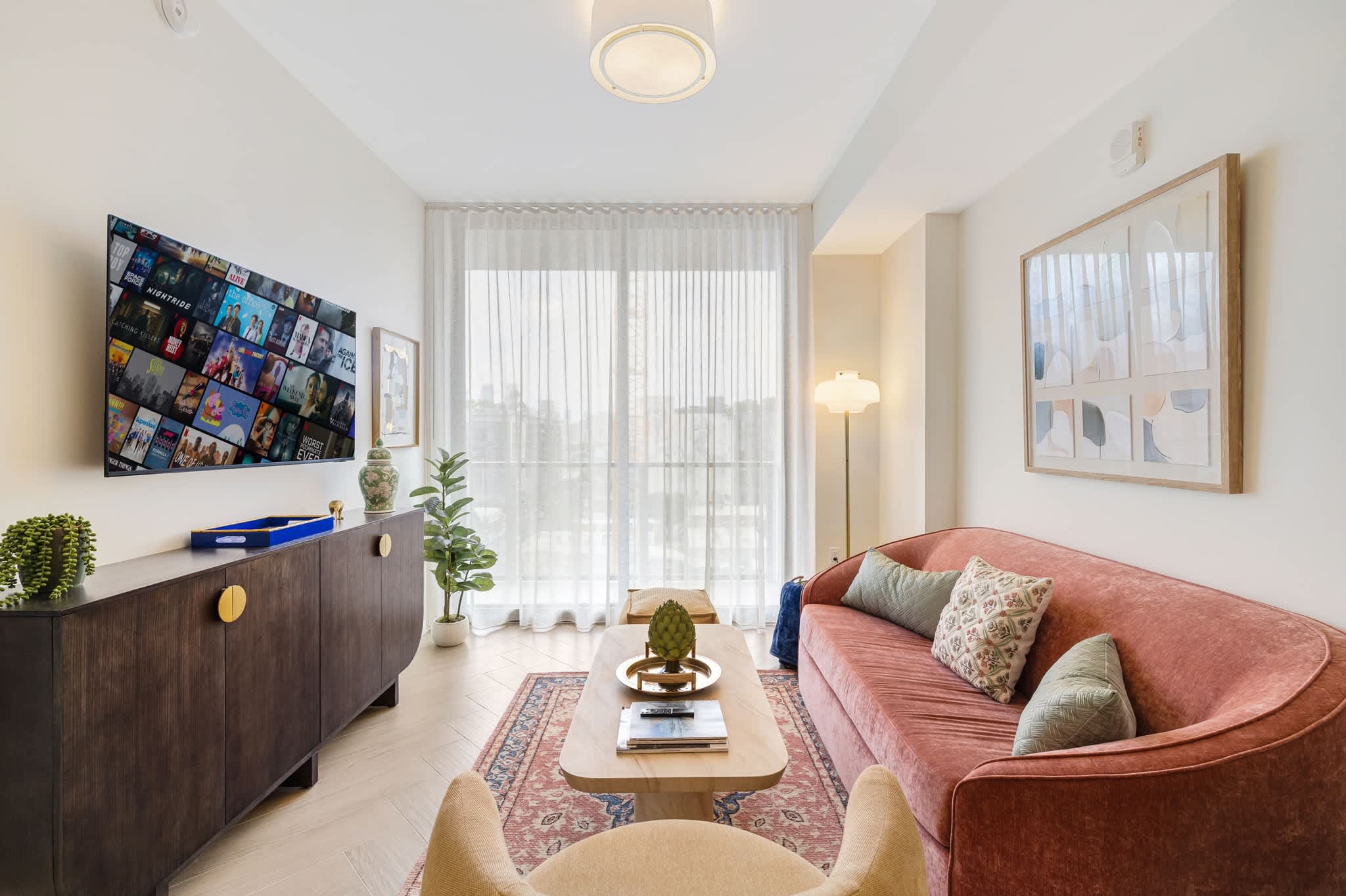 Relax in this chic living room with a cozy velvet sofa, streaming TV, and abundant natural light from floor-to-ceiling windows.