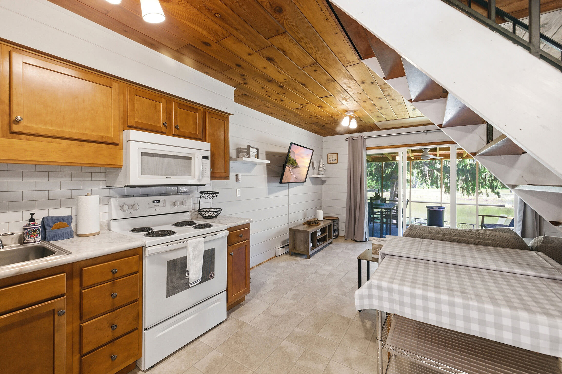 Open-plan kitchen and dining area with full appliances, TV, and direct access to the screened porch for easy flow between cooking, eating, and outside.