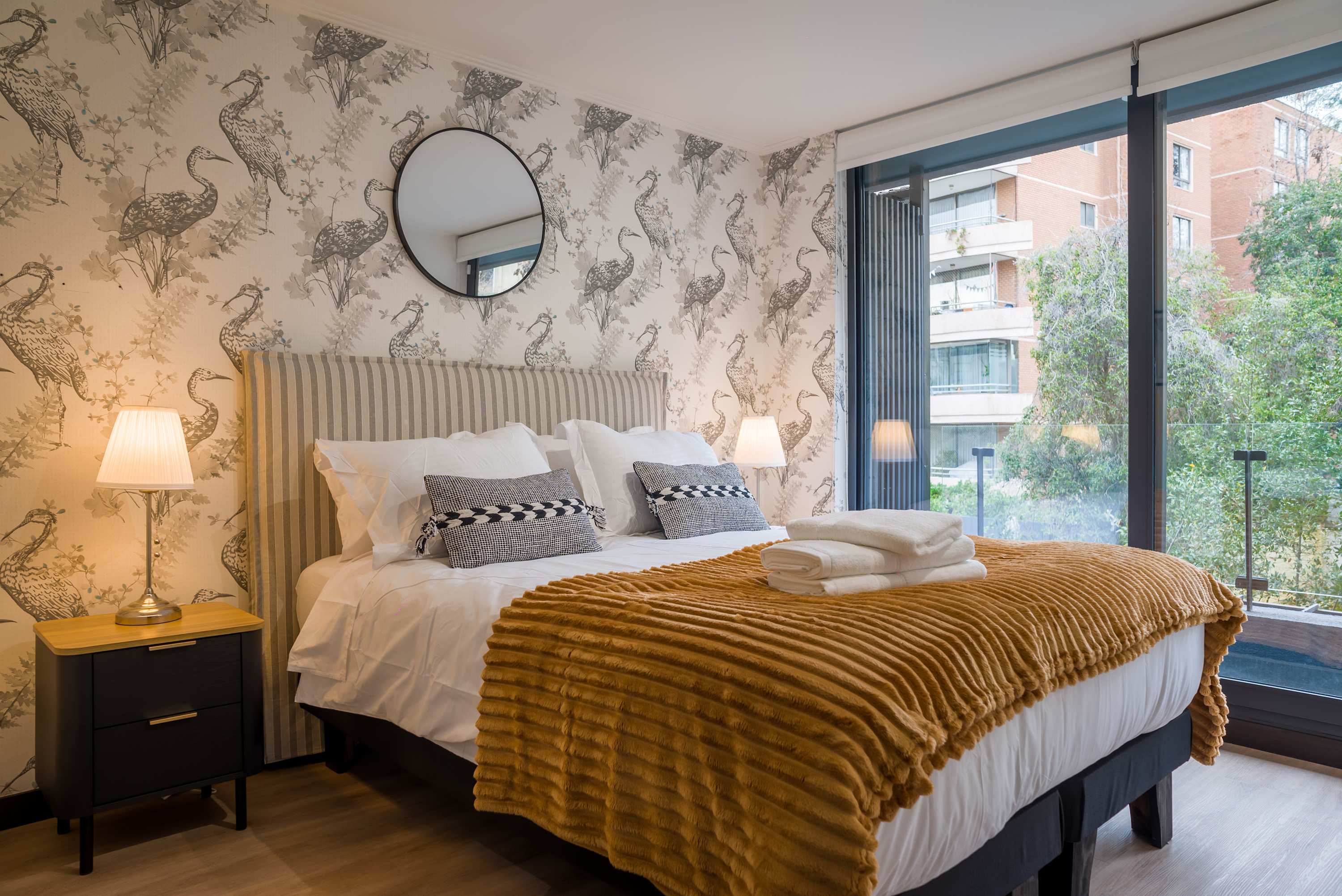 Relax in this stylish bedroom with a cozy bed, chic decor, and a serene view through large windows.