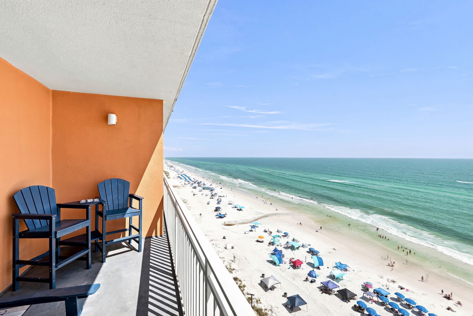 Splash 804E – Balcony with two chairs overlooking a beach and ocean view with umbrellas and people on the sand.