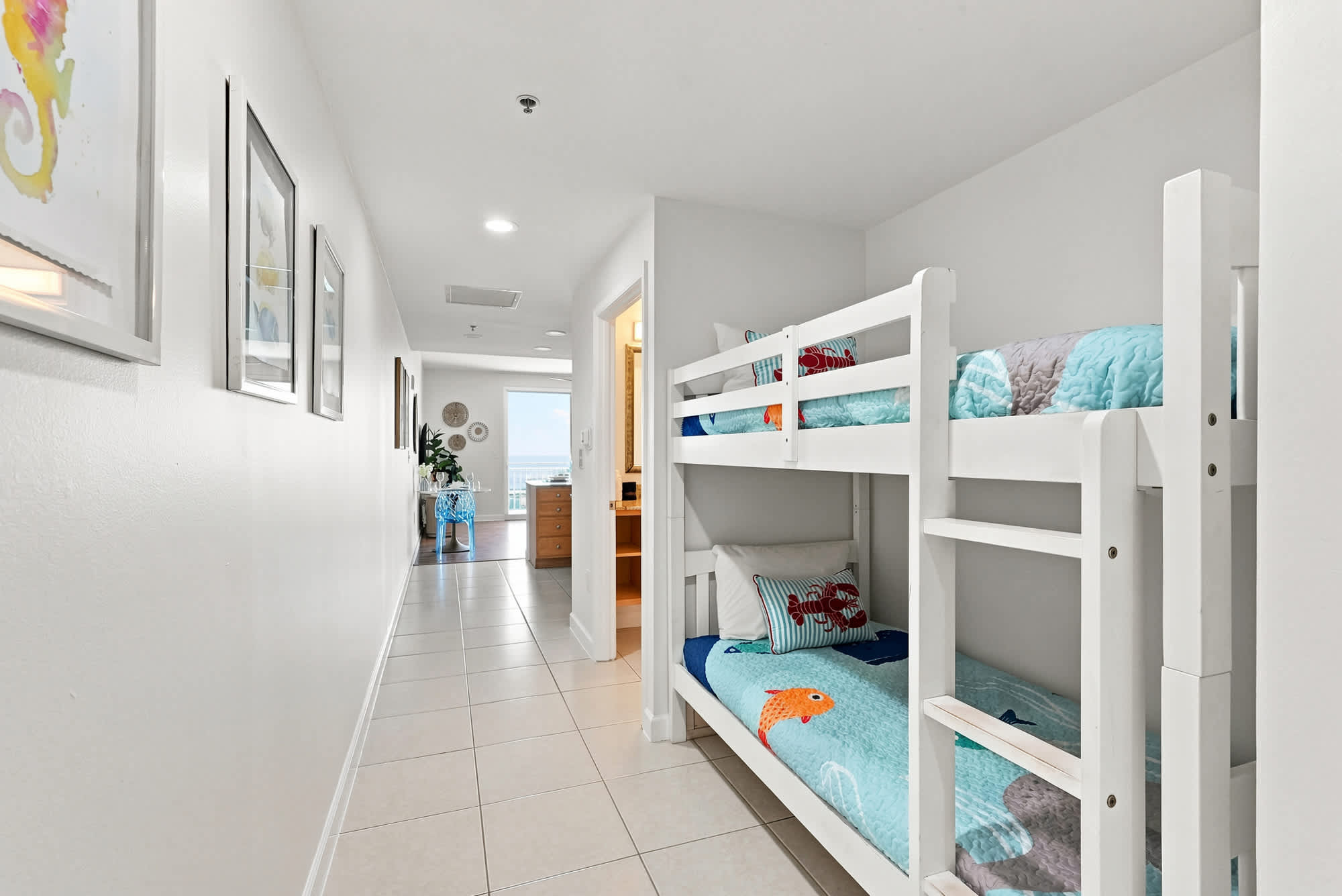 Splash 804E – Bunk beds with colorful bedding in a hallway leading to a bright room with a beachfront view.