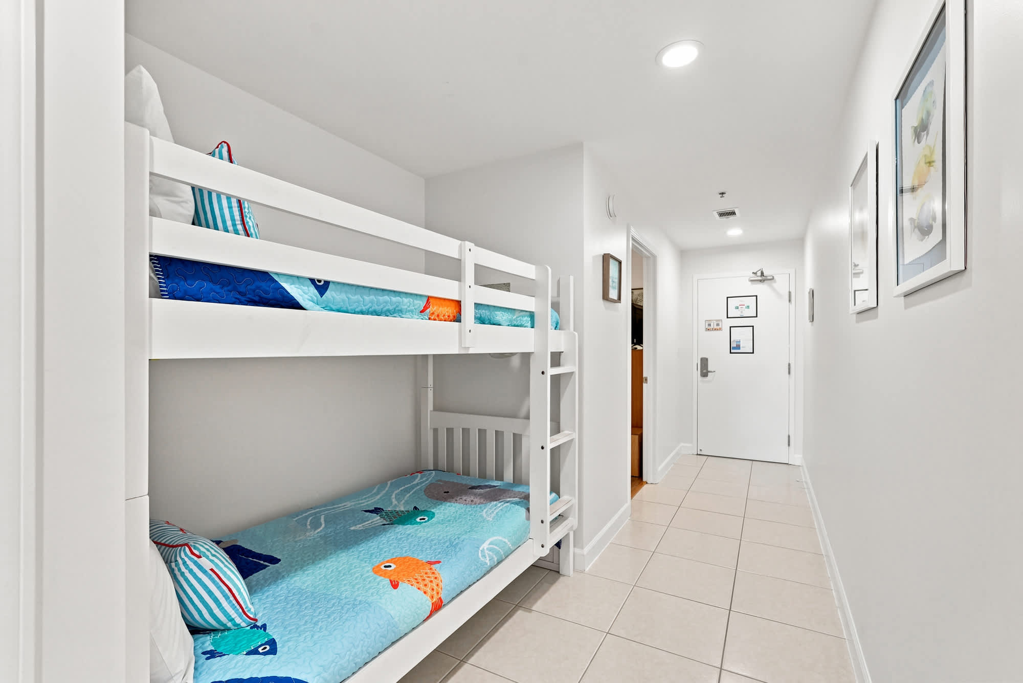 Splash 804E – Bunk beds with colorful fish-themed bedding in a hallway. Light walls and tiled floor.
