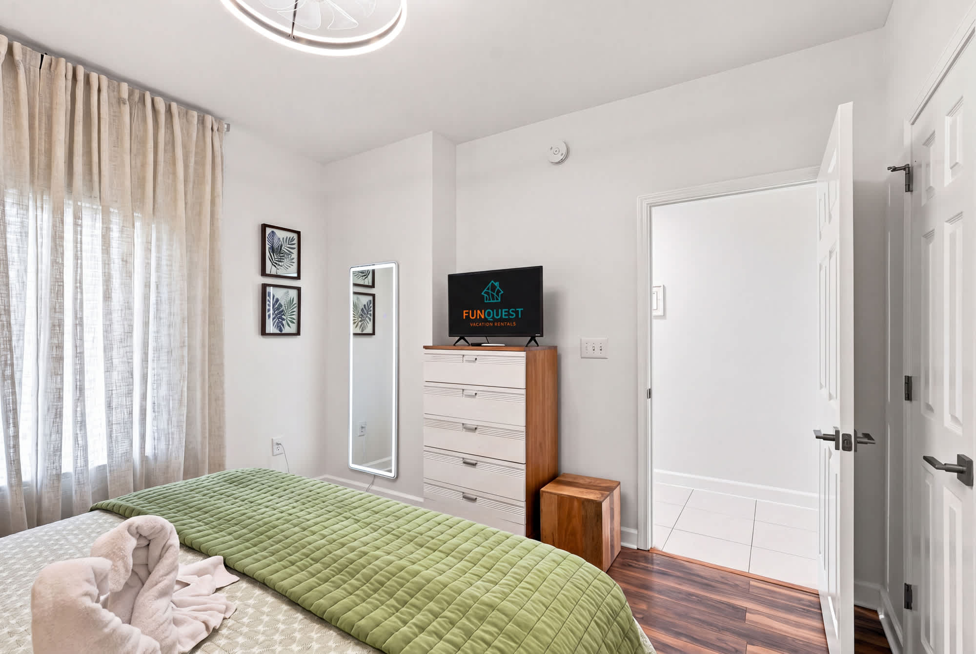 Splash 804E – Bedroom featuring a green quilt, dresser, TV, mirror, and soft lighting from a chandelier.