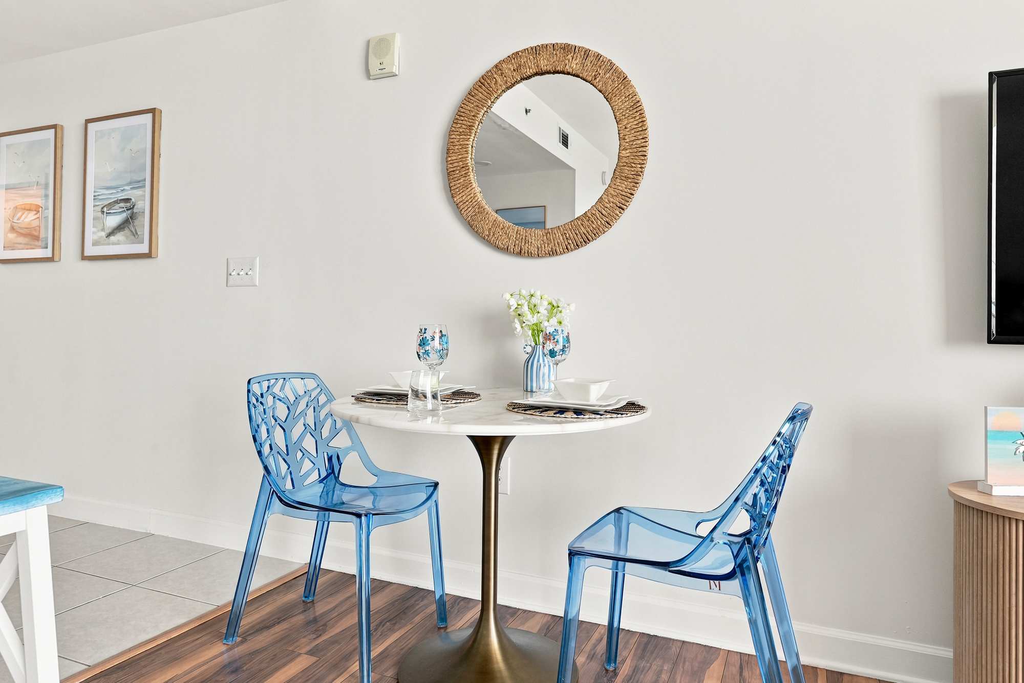 Splash 804E – Dining area with a round table, blue transparent chairs, mirror, and decorative flowers.