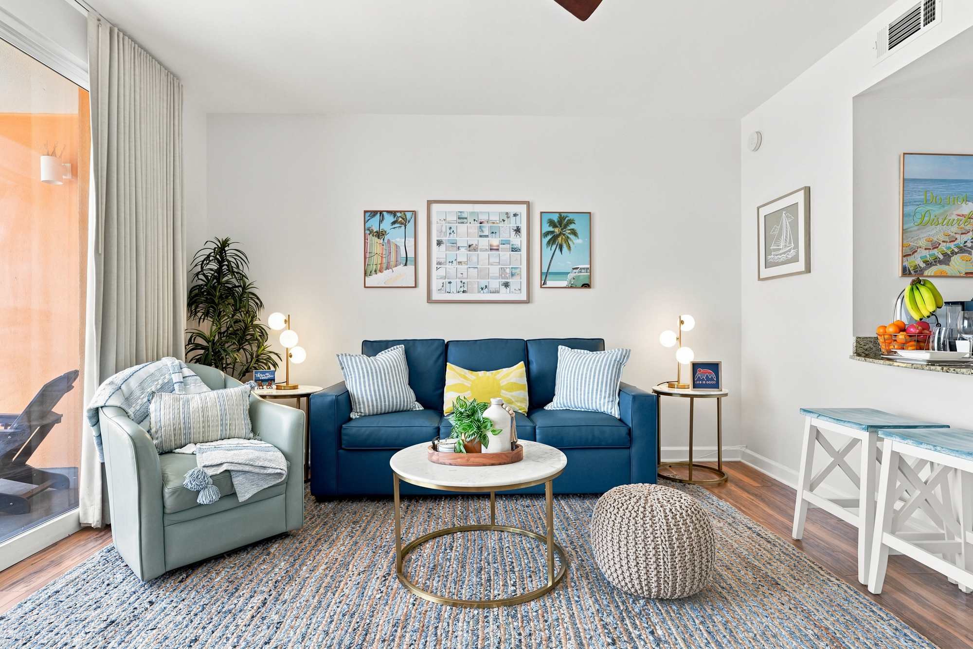 Splash 804E – Cozy living room with blue couch, armchair, round coffee table, and kitchen bar with fruit.