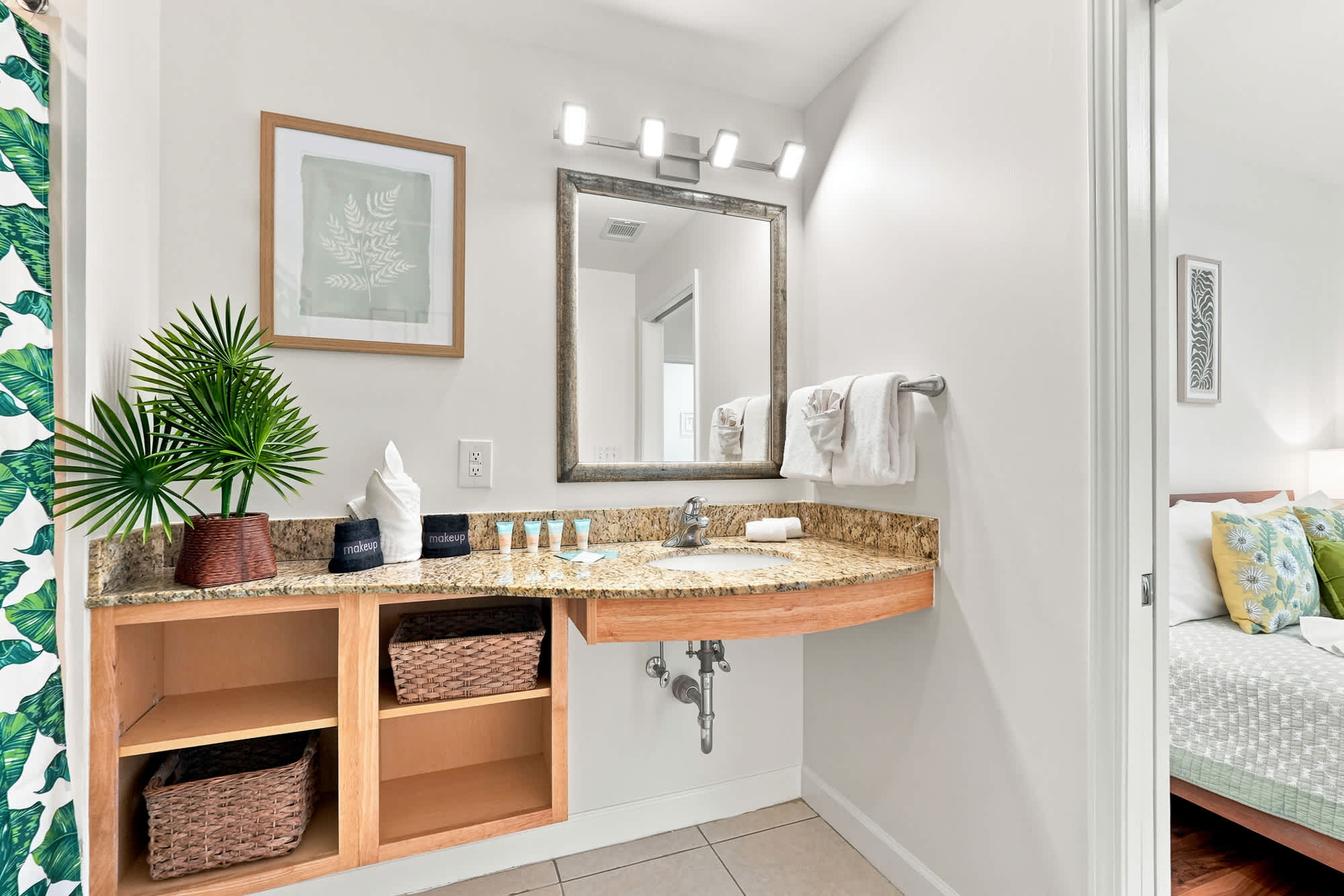 Splash 804E – Bathroom with granite countertop, mirror, decorative plants, and view of a bedroom in the background.