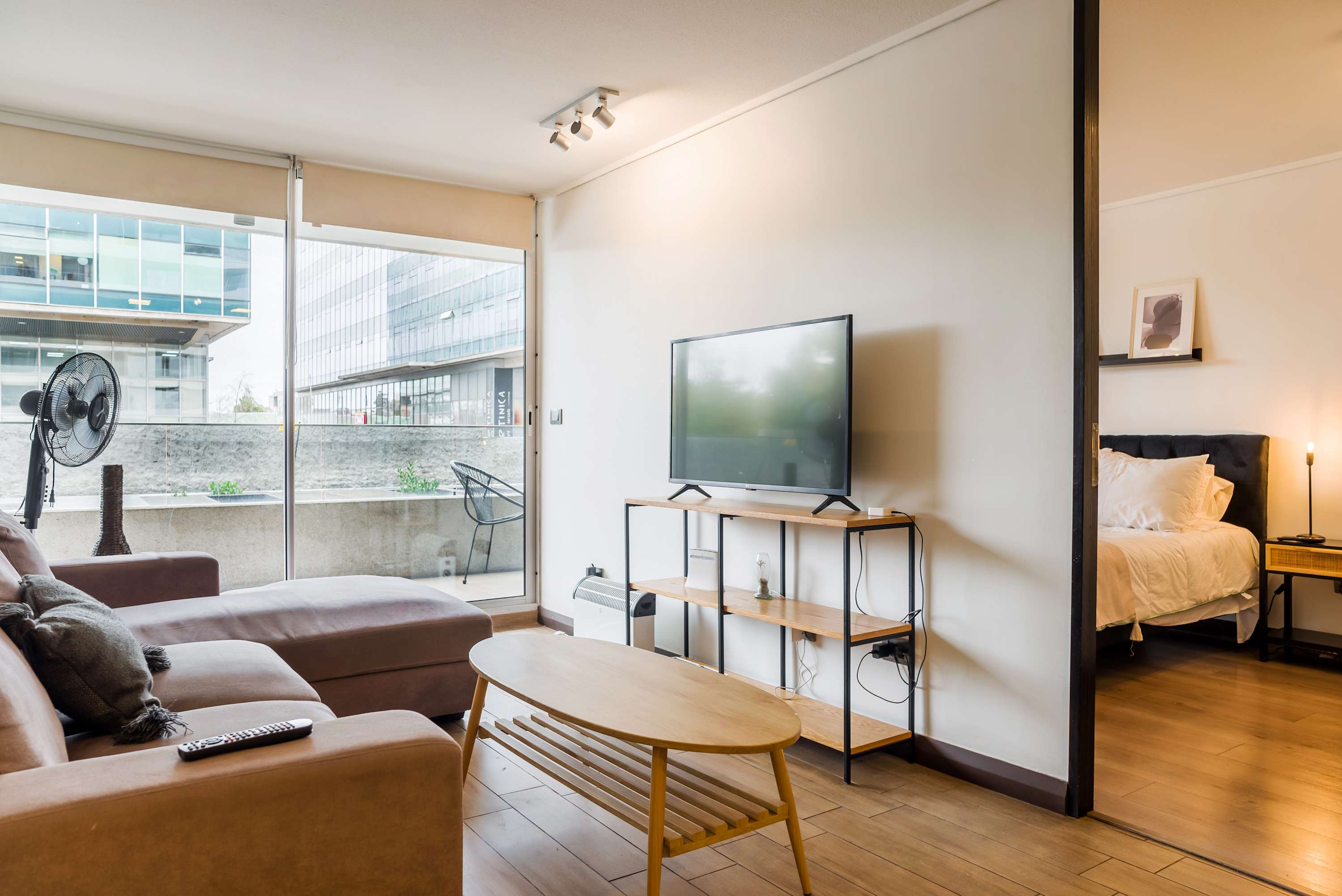 Modern living room with a spacious sectional, flat-screen TV, and floor-to-ceiling windows opening to a furnished balcony and city views.