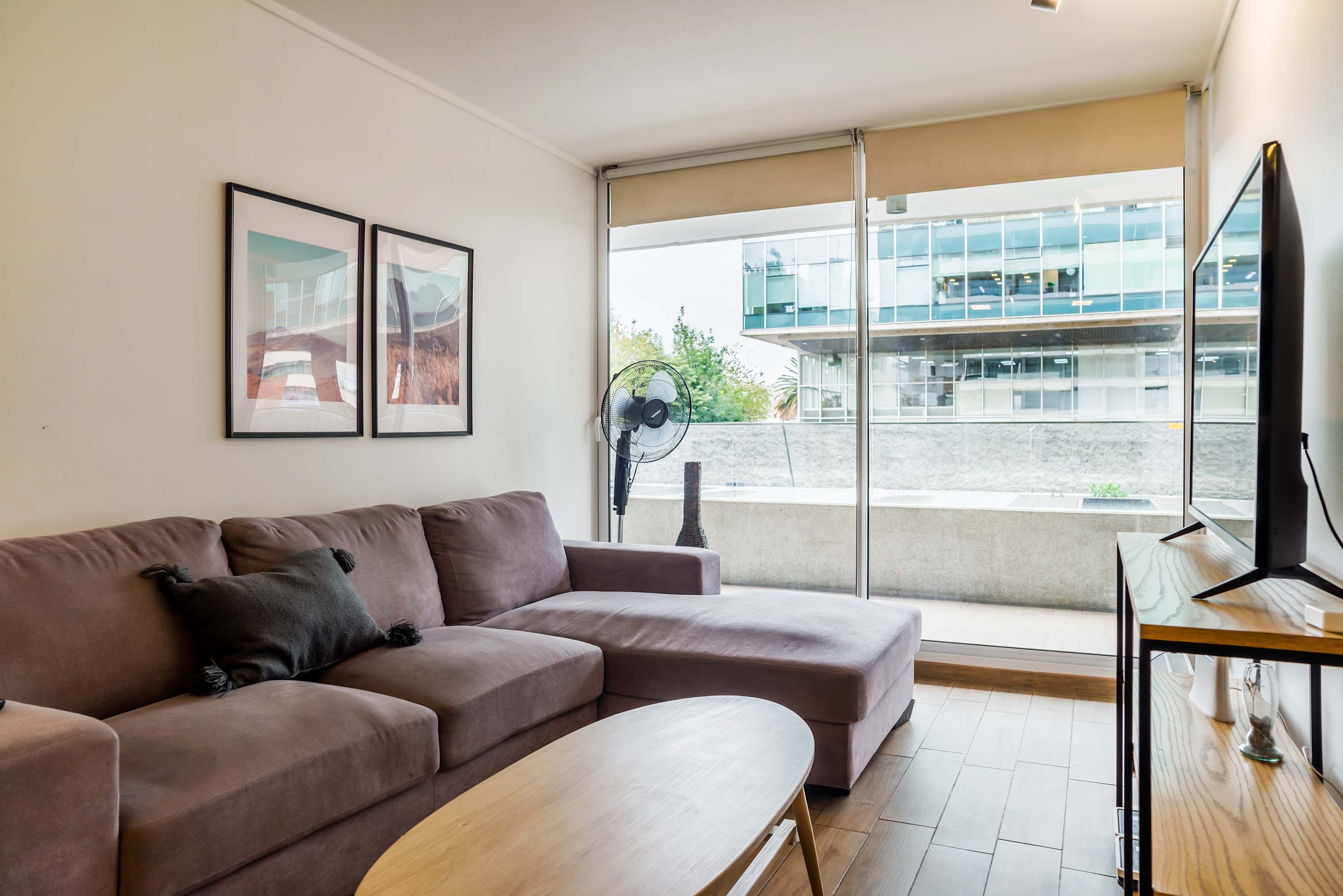 Private living room with a spacious sectional sofa, oval wood coffee table, and floor-to-ceiling corner windows overlooking a modern courtyard.