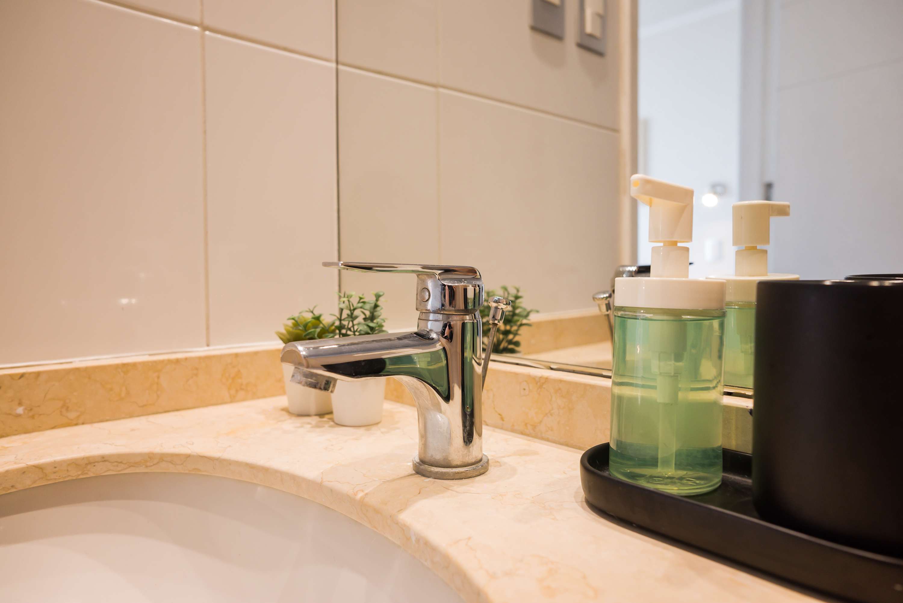 Private bathroom vanity with a polished chrome faucet, cream marble countertop, integrated sink, and neatly arranged toiletries.