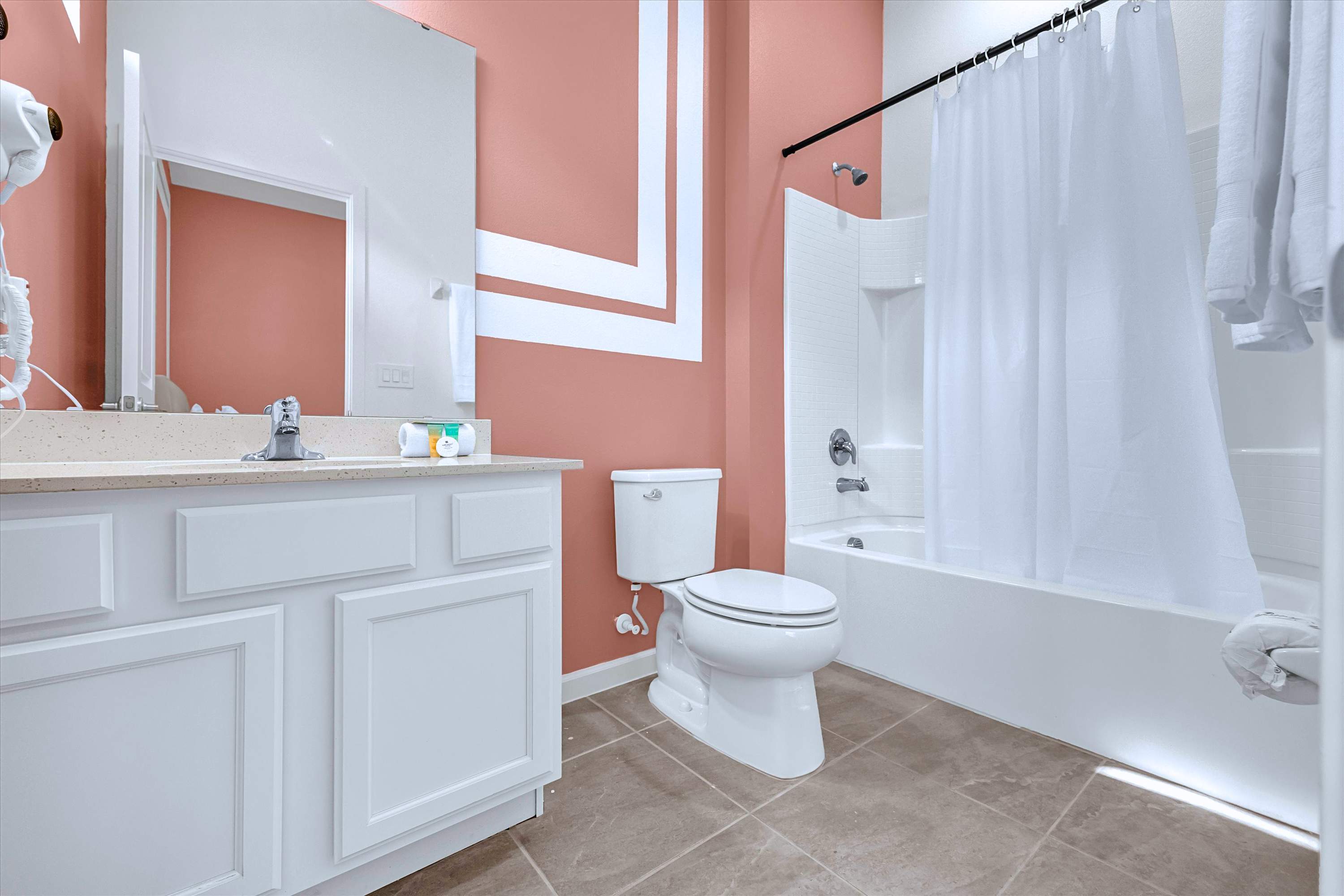 Pink room en-suite bath equipped with bathtub shower combo, sink vanity, mirror & toilet