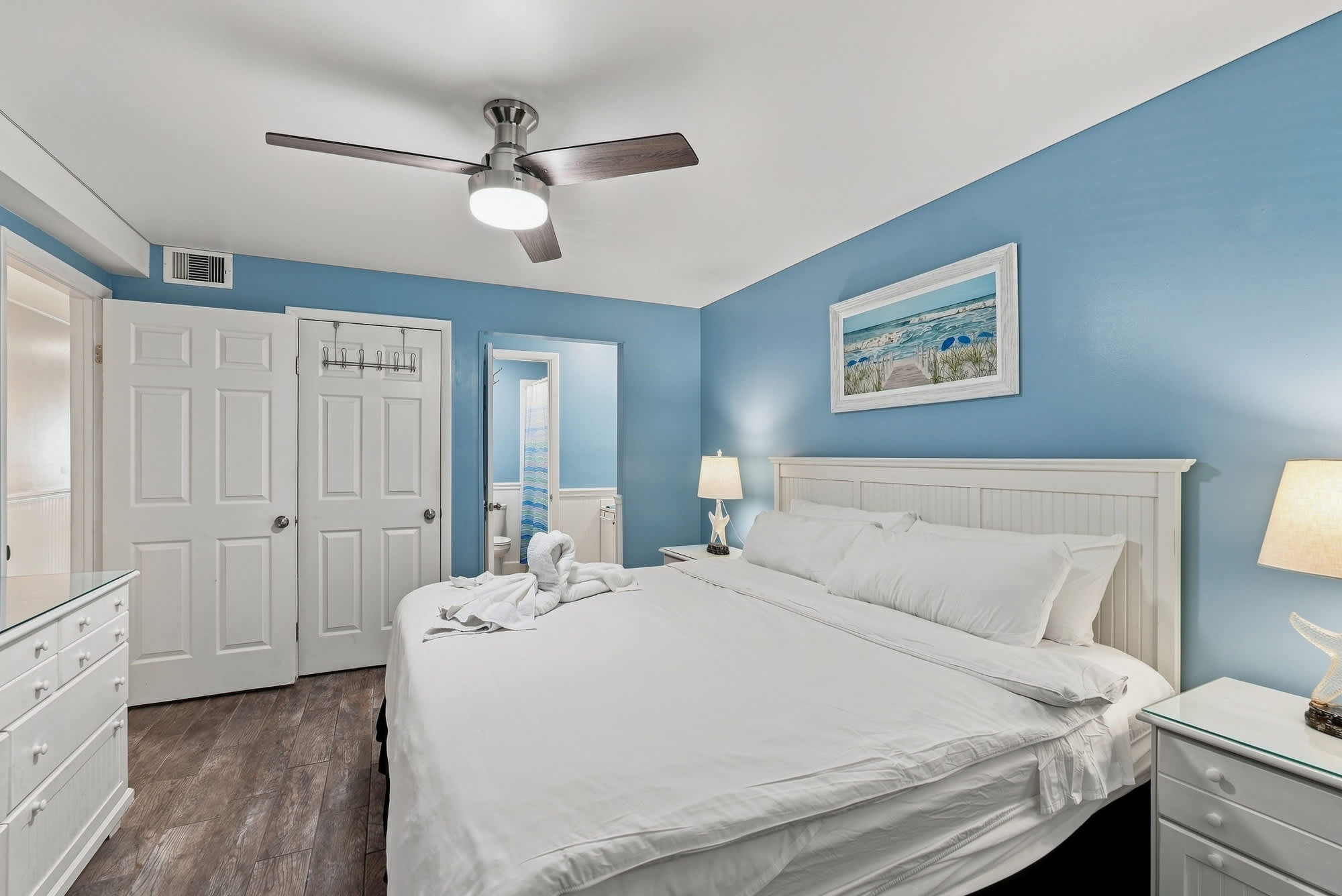 The Summit 308  – Bedroom with a king bed, blue walls, dresser, lamp, and adjoining bathroom access.