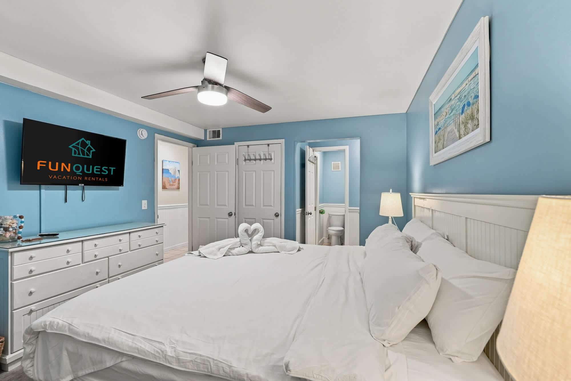 The Summit 308  – Bedroom with a queen bed, dresser, TV, and private bathroom door visible. Blue walls and decorative artwork.