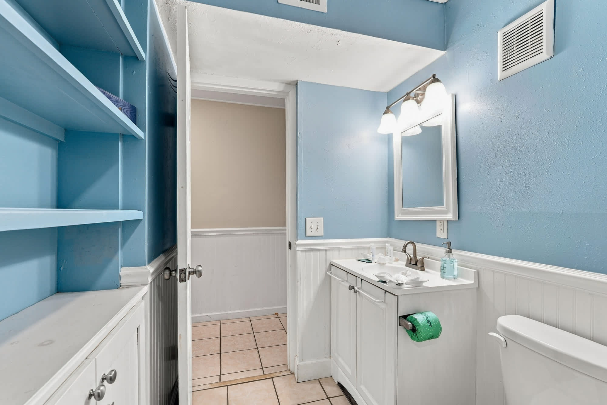 The Summit 308  – Bathroom with blue walls, white vanity, mirror, and tile flooring, featuring a toilet and open shelving.