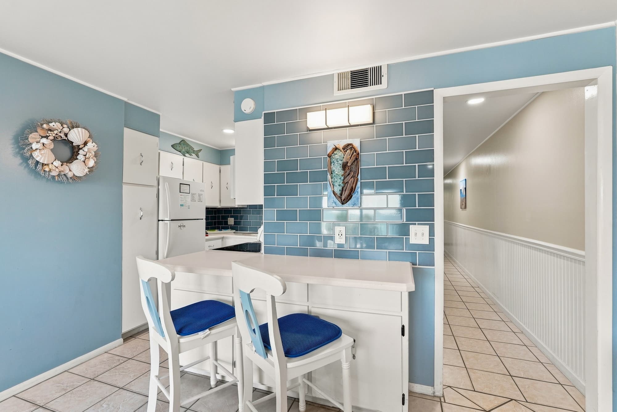 The Summit 308  – Bright kitchen with white cabinets, blue backsplash, two bar stools, and a hallway leading out.