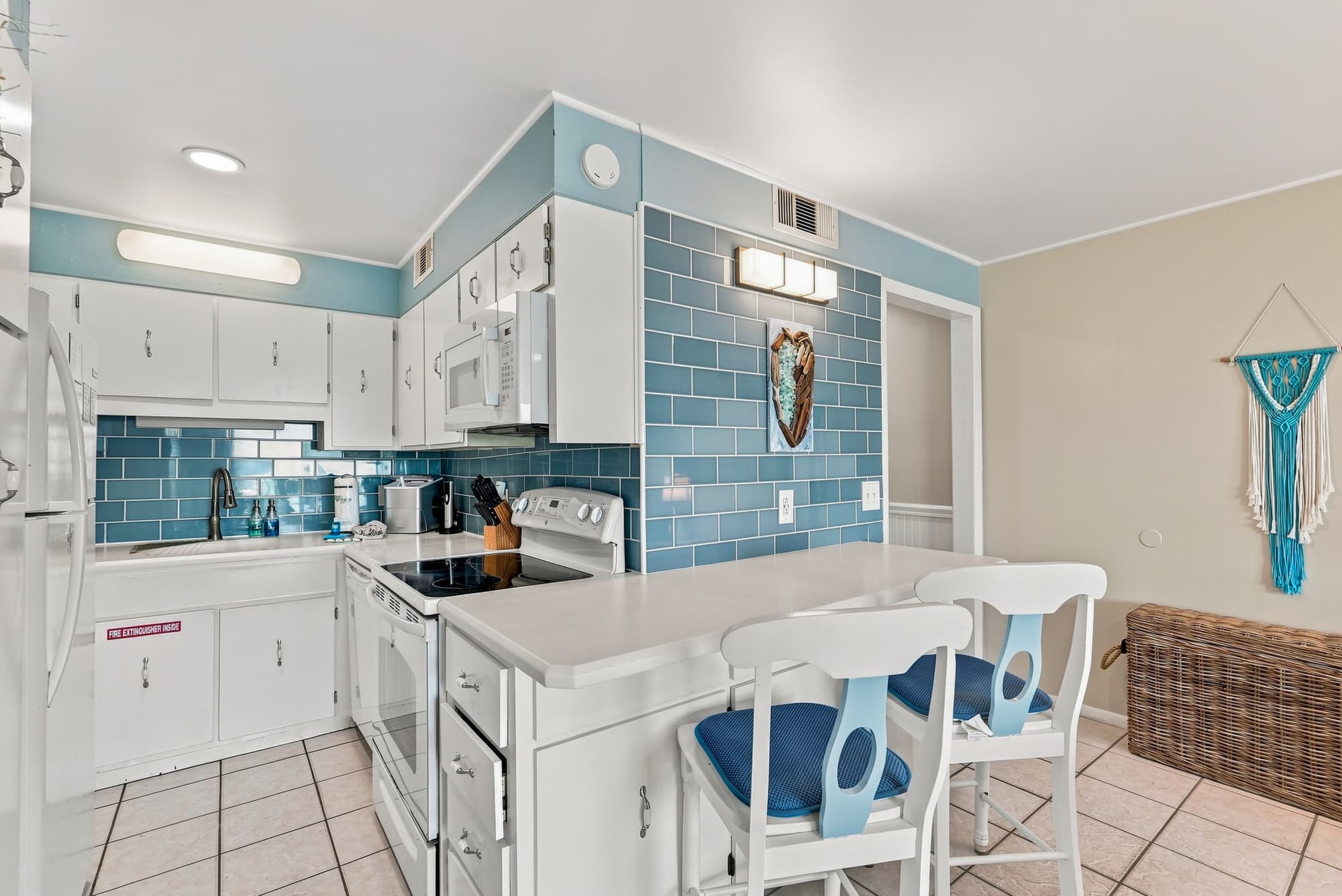 The Summit 308  – Bright kitchen with white cabinets, blue tile backsplash, bar seating, and decorative wall hanging.