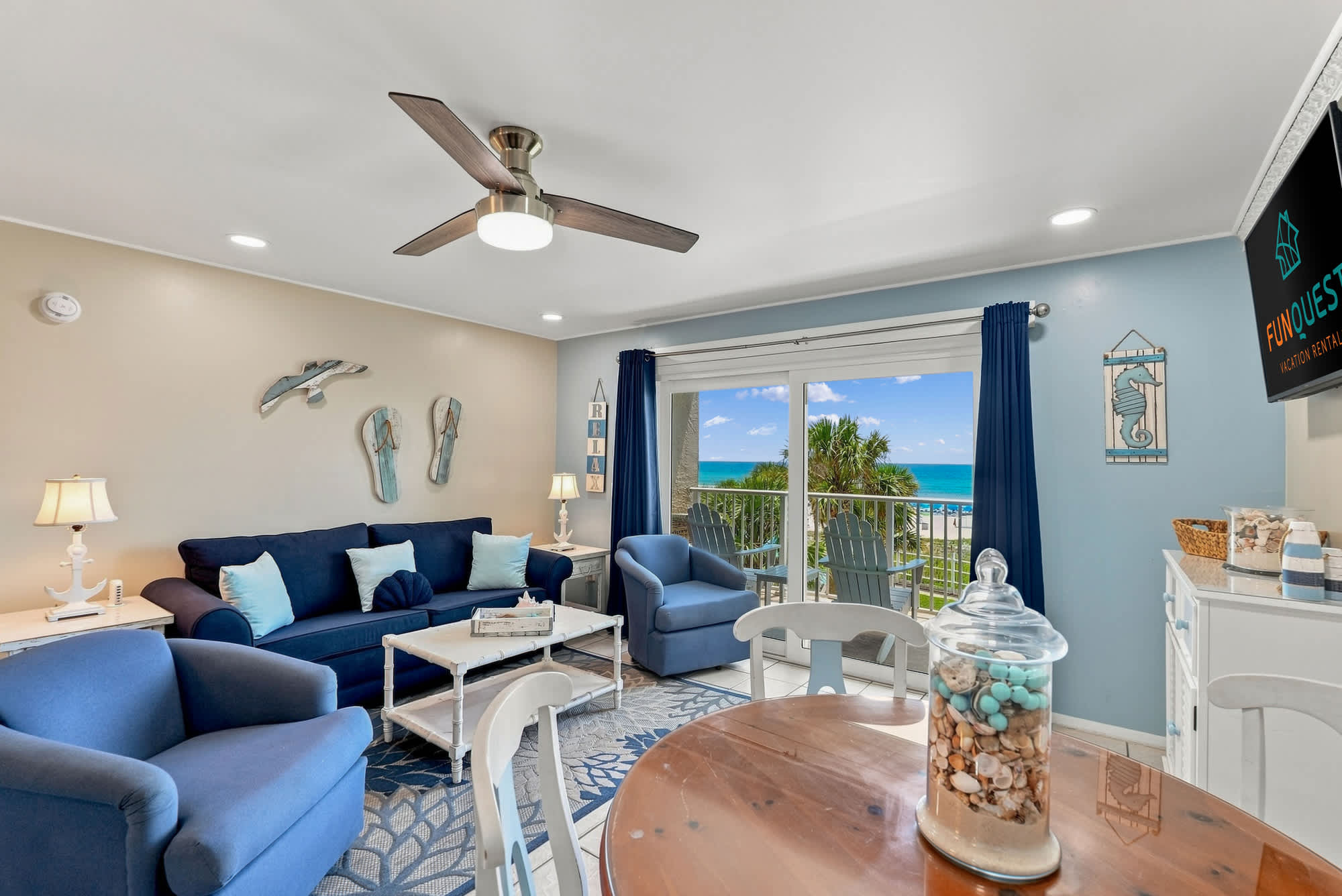 The Summit 308  – Cozy living room with blue furniture, dining table, and ocean view through sliding glass doors.