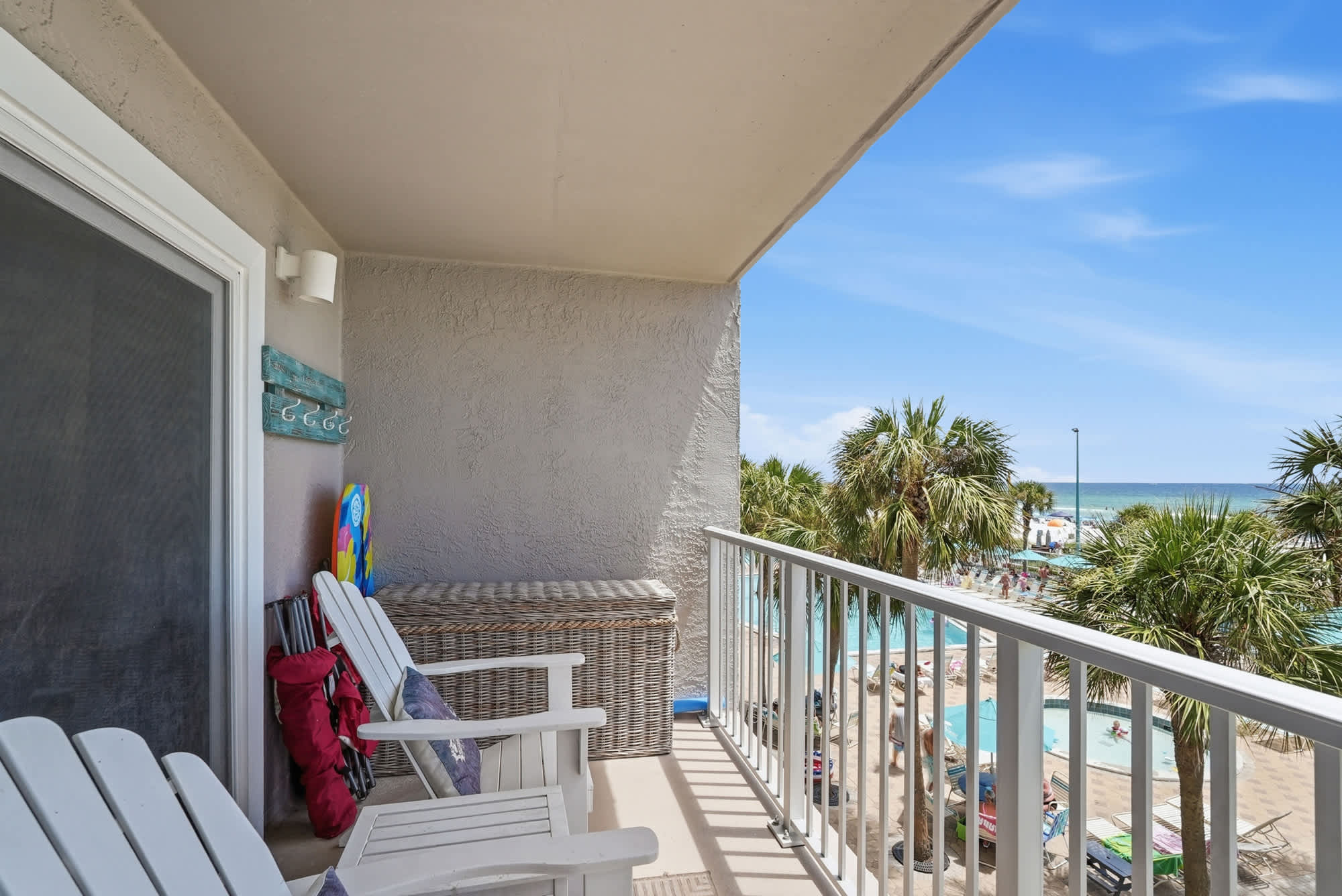 The Summit 308  – Balcony view with white chairs, palm trees, and swimming pool overlooking the beach.