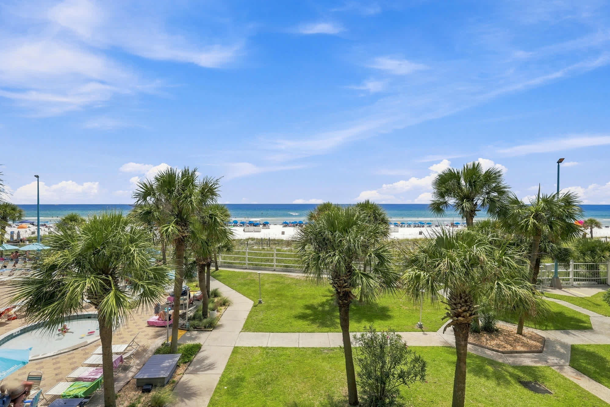 The Summit 308  – View of a beach with palm trees and a pool area under a blue sky at The Summit 308.
