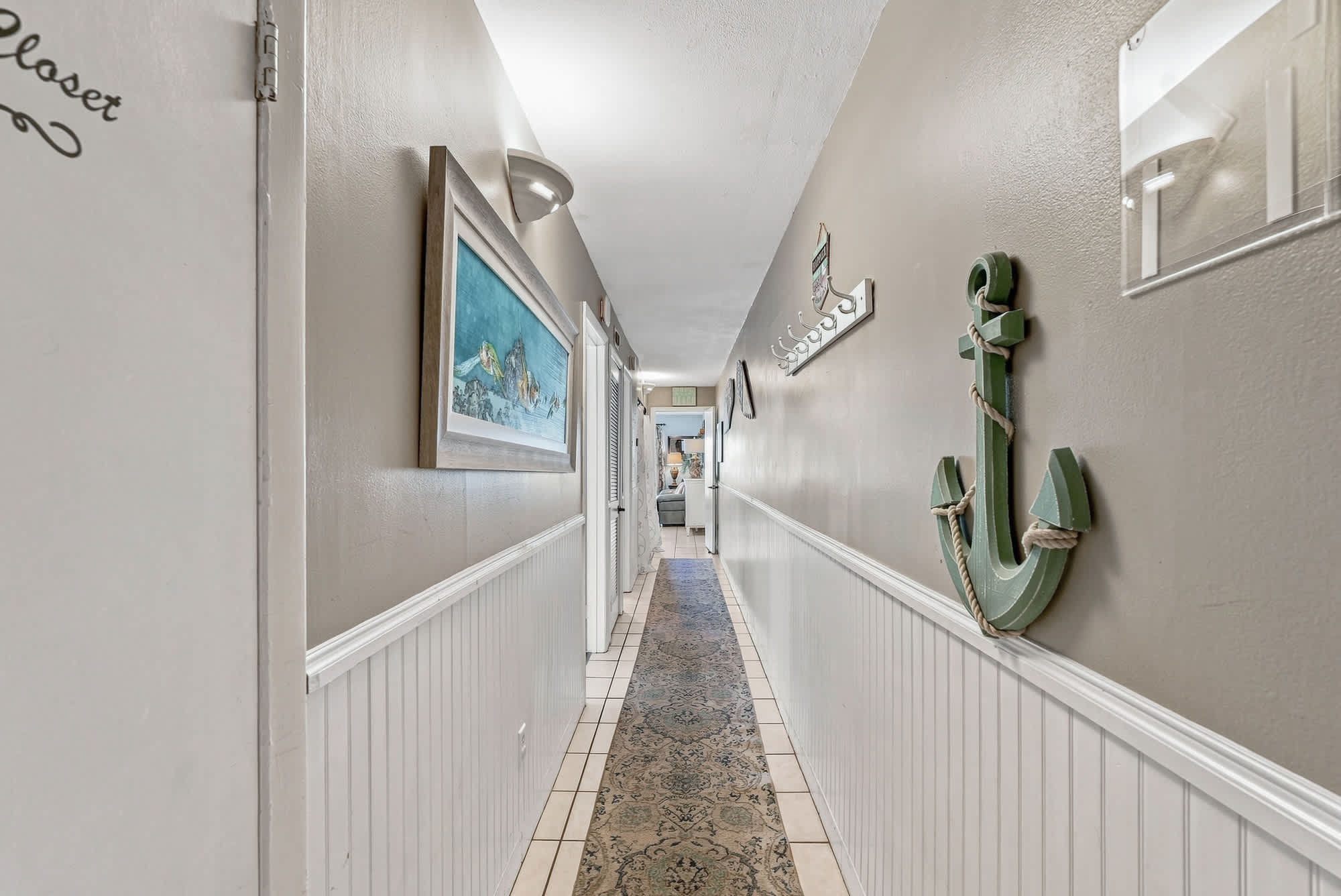 The Summit 225 – Narrow hallway with wall art, light fixtures, decorative anchor, and a patterned runner rug.