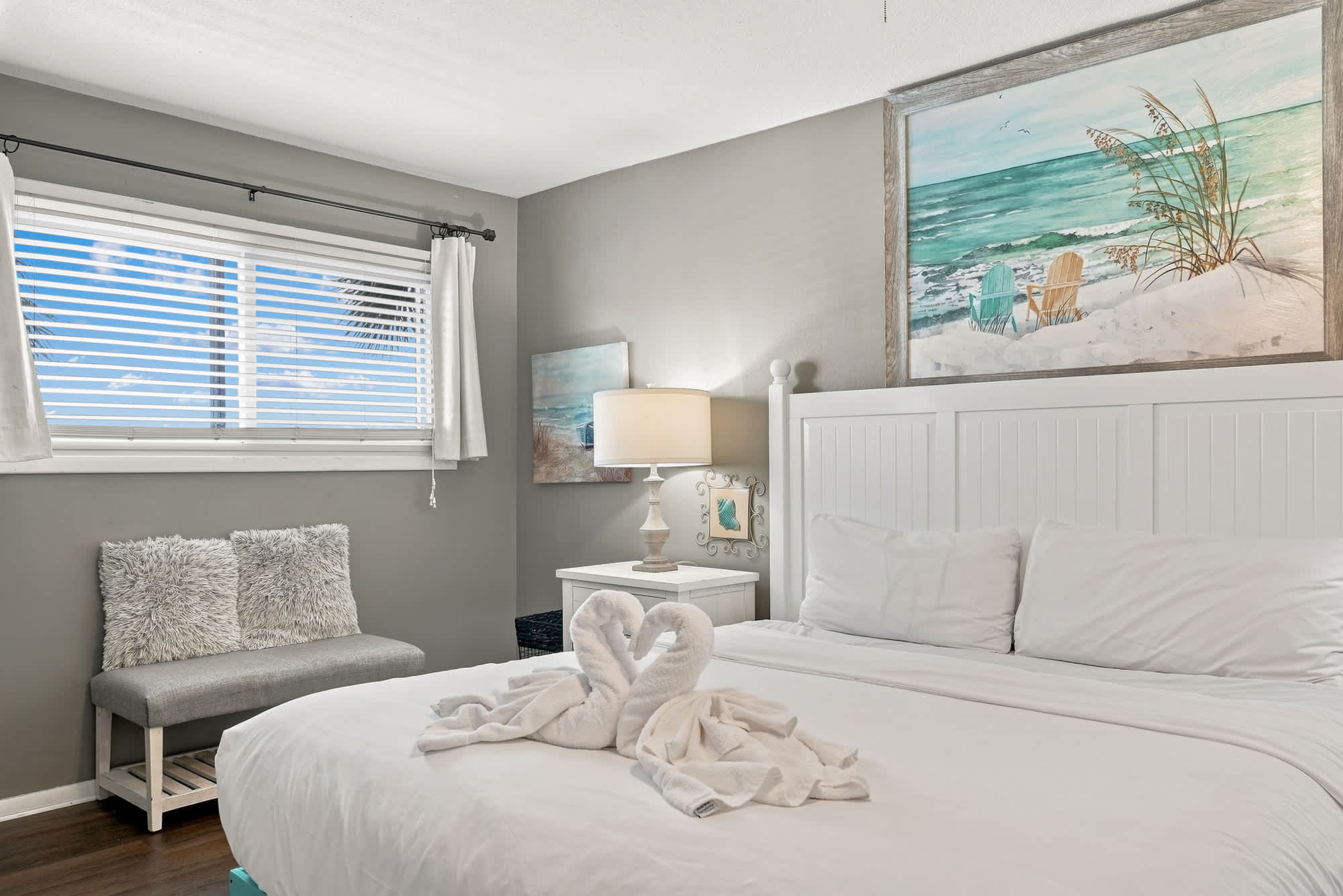 The Summit 225 – Cozy bedroom featuring a white bed, lamp, artwork, decorative towels, and a bench by the window.