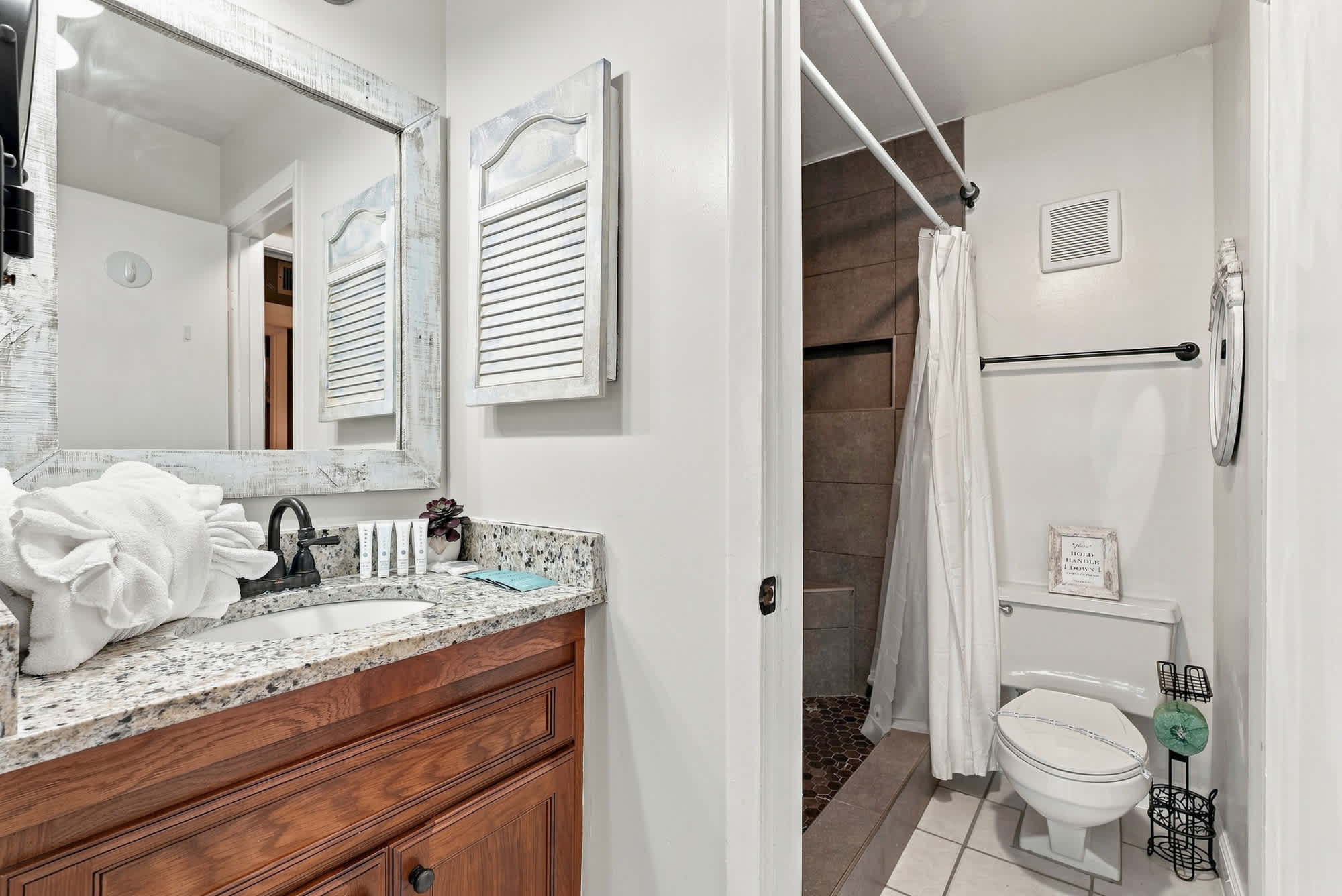The Summit 225 – Bathroom with granite countertop, mirror, shower, and wooden vanity. White towels and toiletries on the counter.