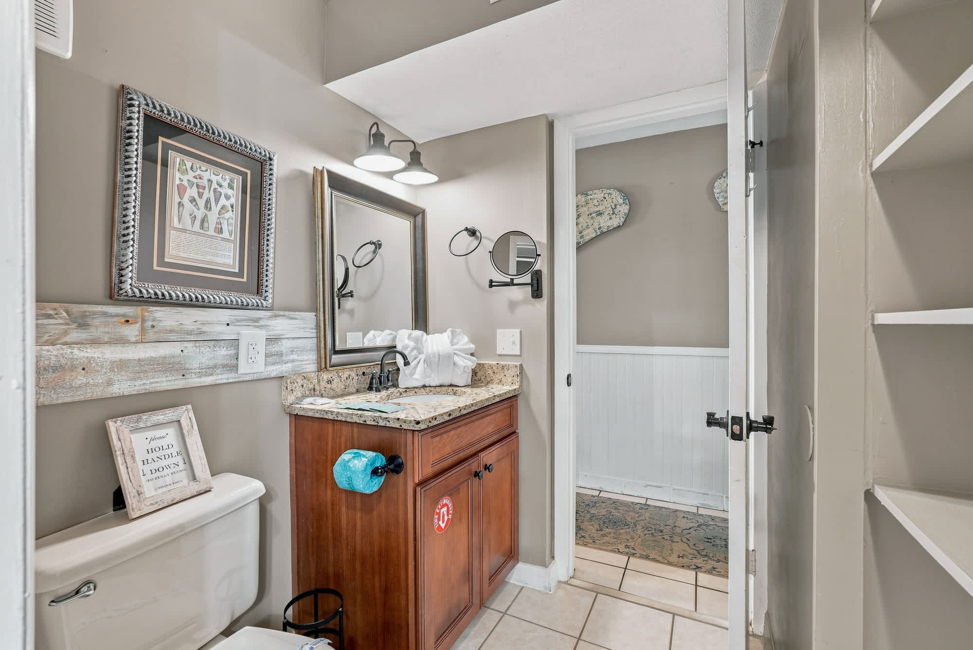 The Summit 225 – Bathroom with granite countertop, mirror, decorative art, and access to a small hallway.