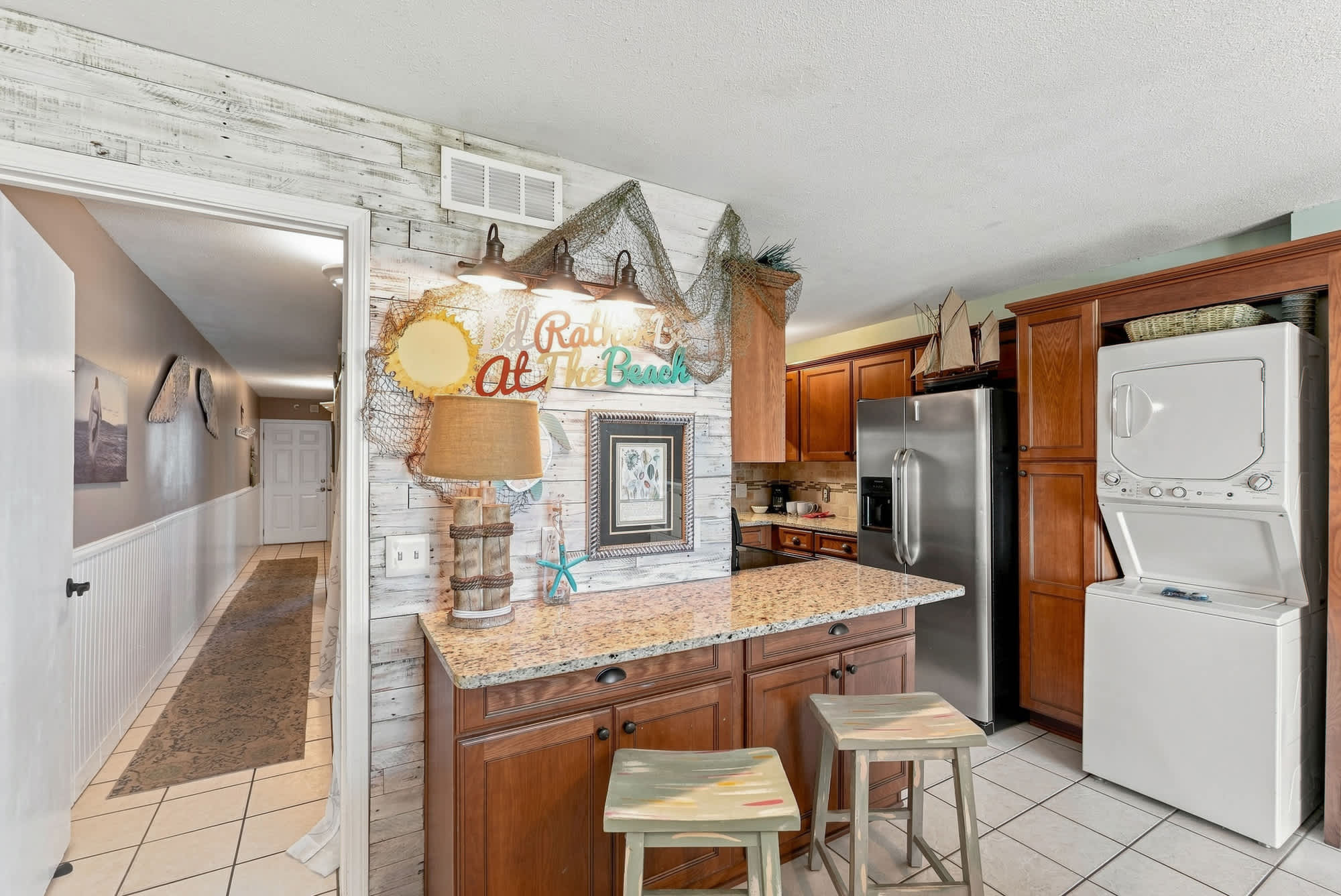 The Summit 225 – Open kitchen with granite countertop, wooden cabinets, two stools, and laundry appliances visible.