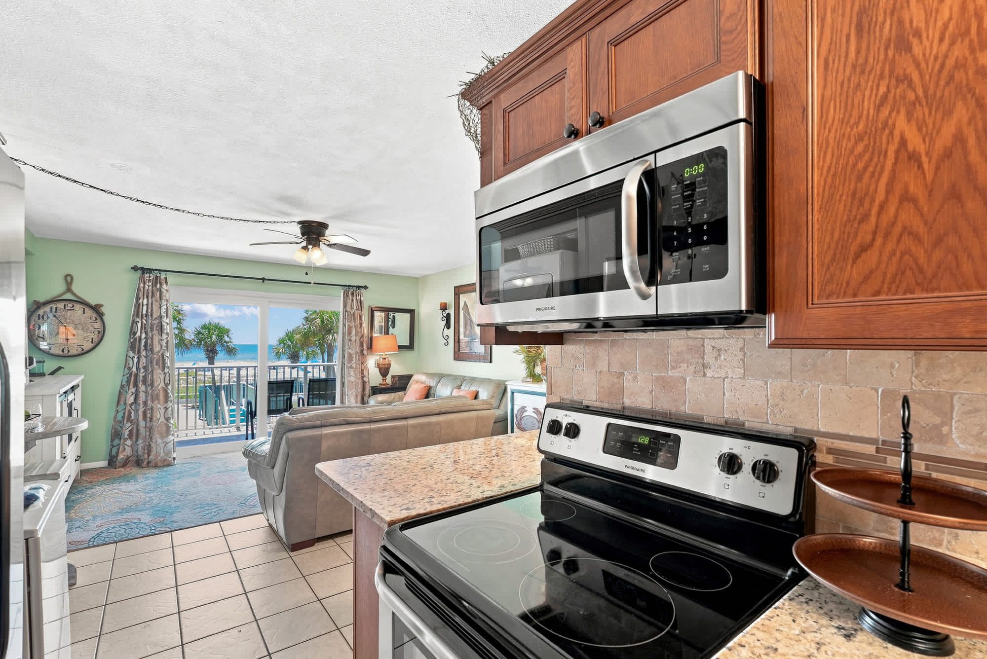 The Summit 225 – Kitchen with stainless steel appliances and granite countertops, overlooking a living area and balcony with ocean view.