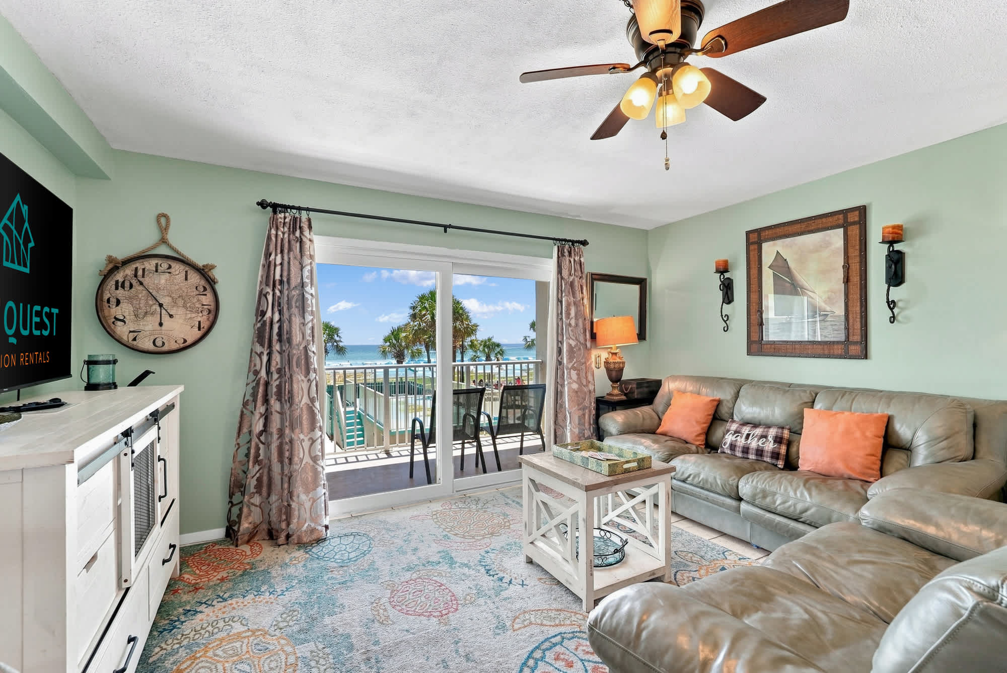 The Summit 225 – Living room with sofa, decorative rug, and balcony view of palm trees and ocean.