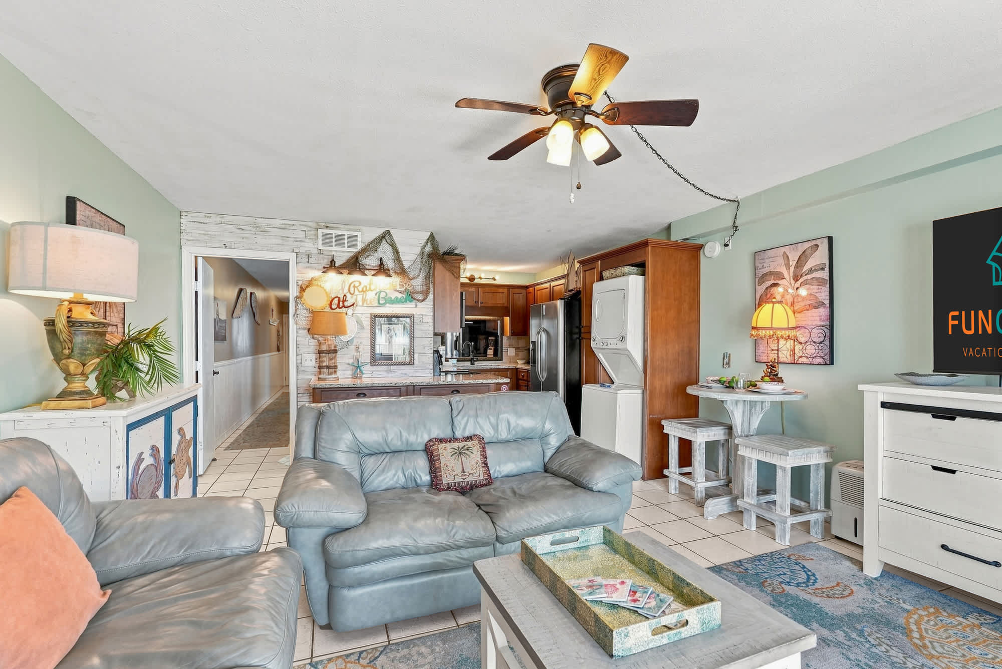 The Summit 225 – Living room with blue couch, ceiling fan, kitchen area, and small dining table.