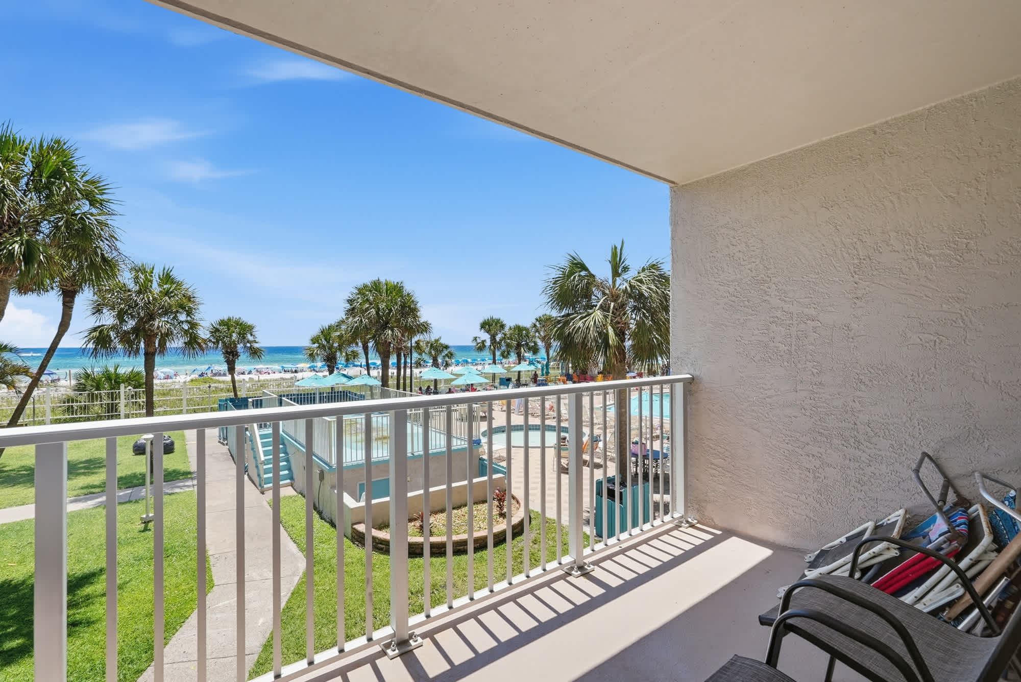 The Summit 225 – Balcony view overlooking a pool area, palm trees, and the ocean in the background.