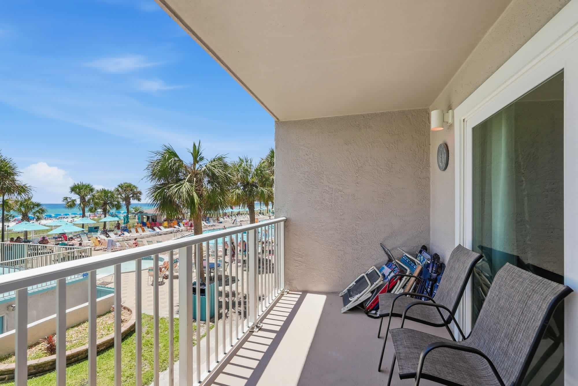 The Summit 225 – Balcony with two chairs overlooking a pool area and beach with sun loungers and palm trees.