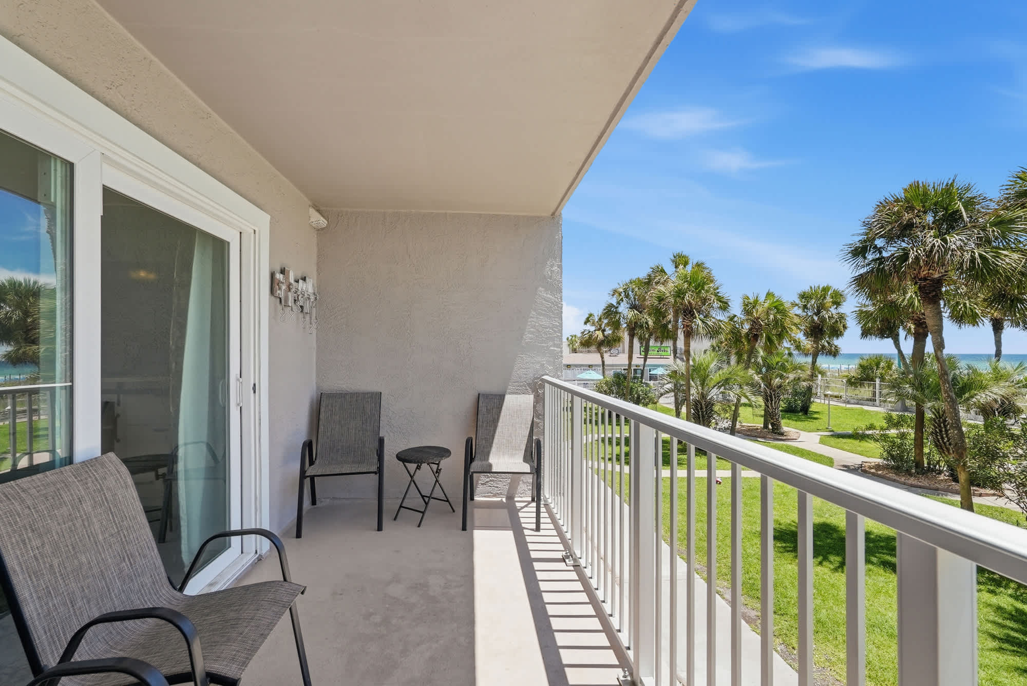 The Summit 225 – Balcony with two chairs and a table, overlooking palm trees and the ocean.