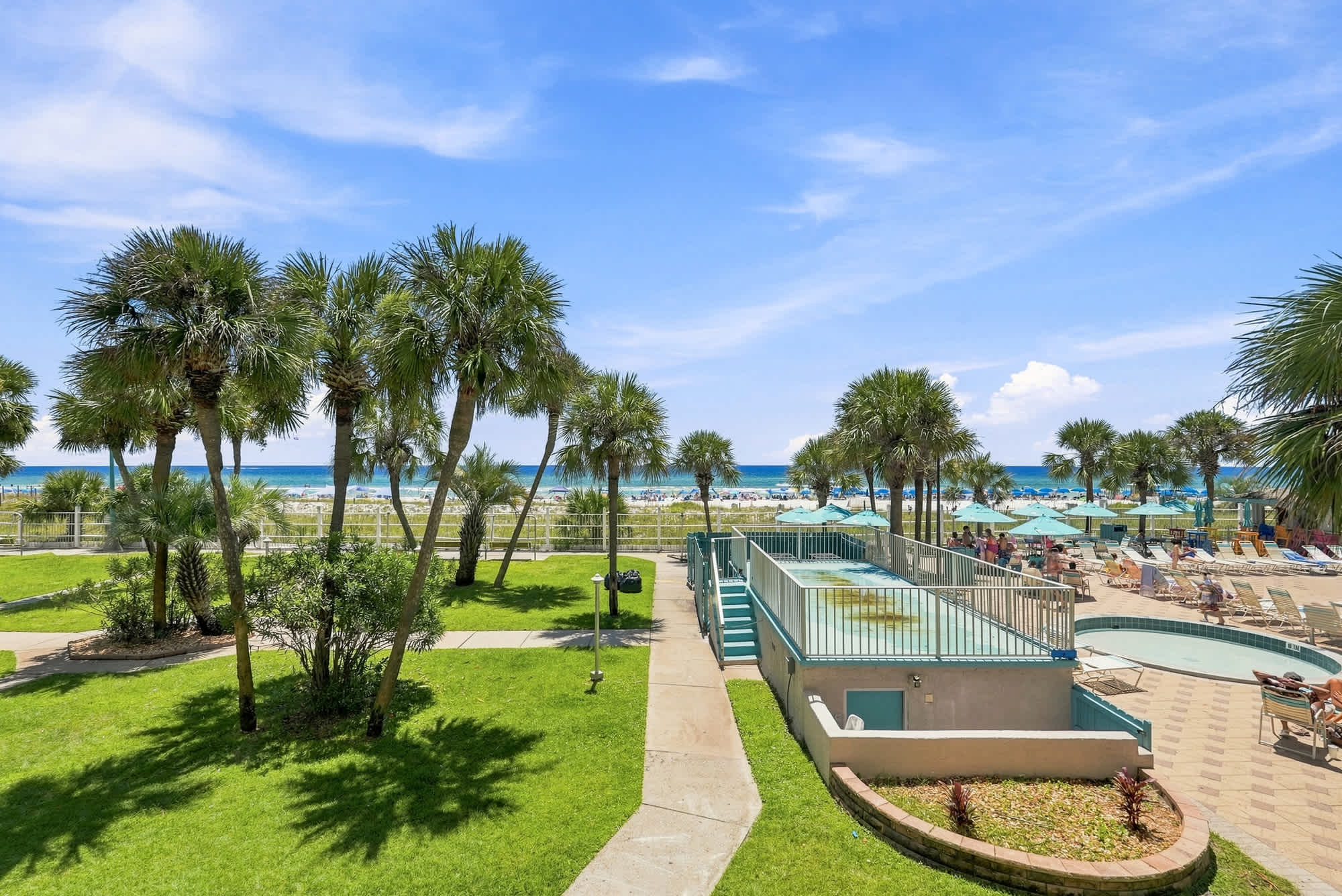 The Summit 225 – View of palm trees, grassy area, pool, and beach with umbrellas in the background.