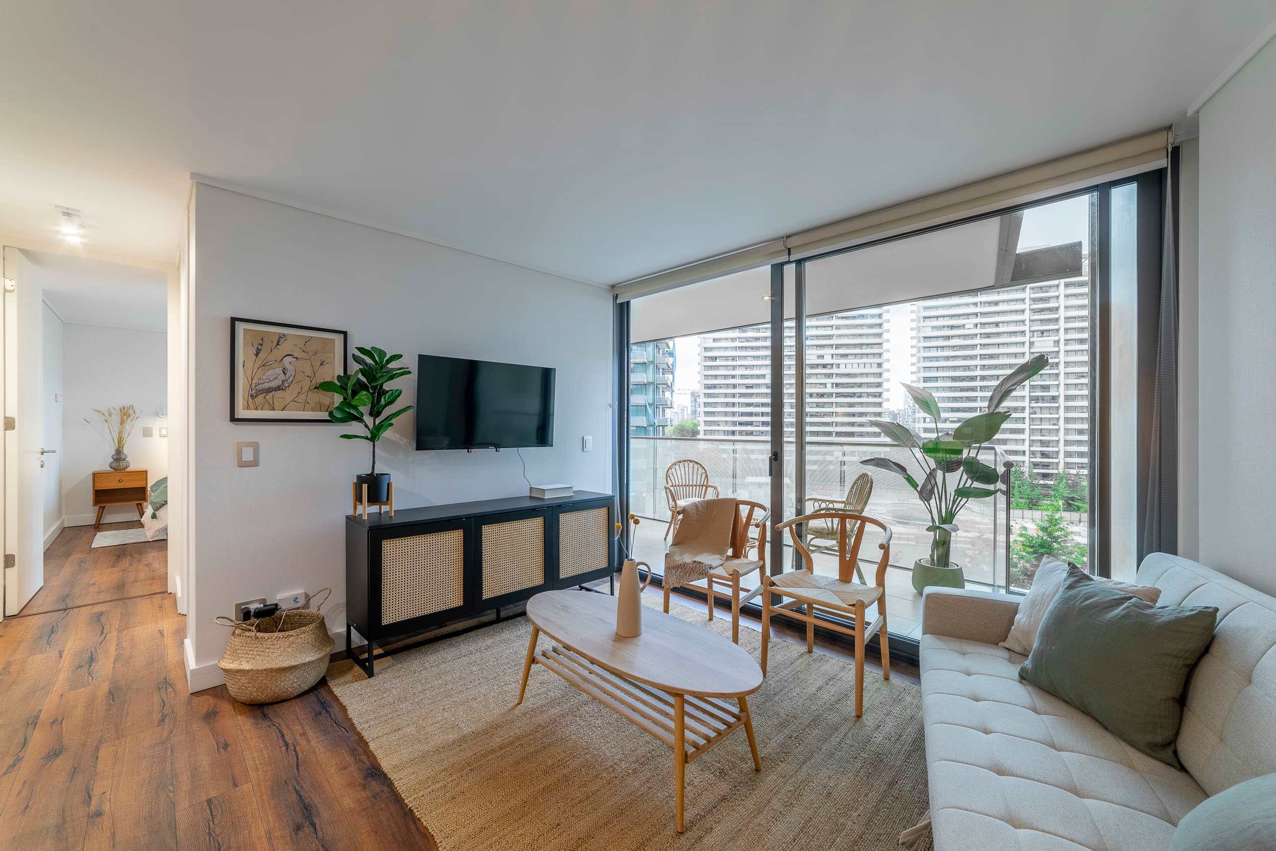 Private living room with floor-to-ceiling windows, city views, natural wood seating, and a leafy balcony setting.