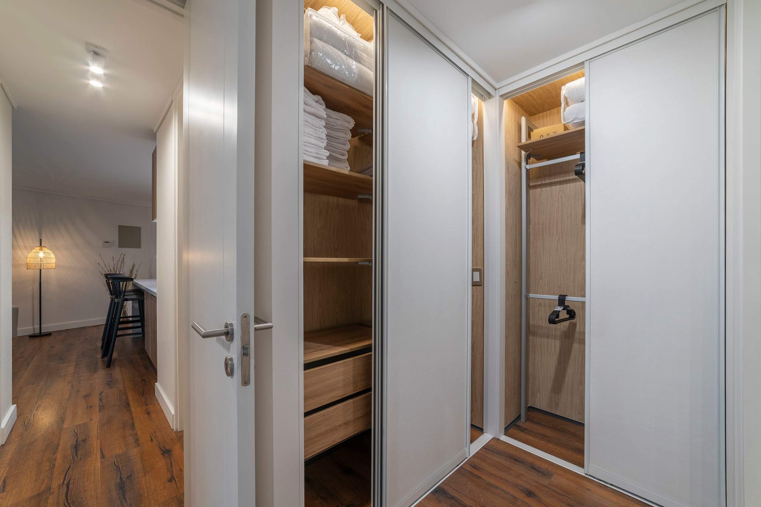 Walk-in dressing area with mirrored wardrobes, warm wood shelving, and neatly arranged linens for convenient storage.
