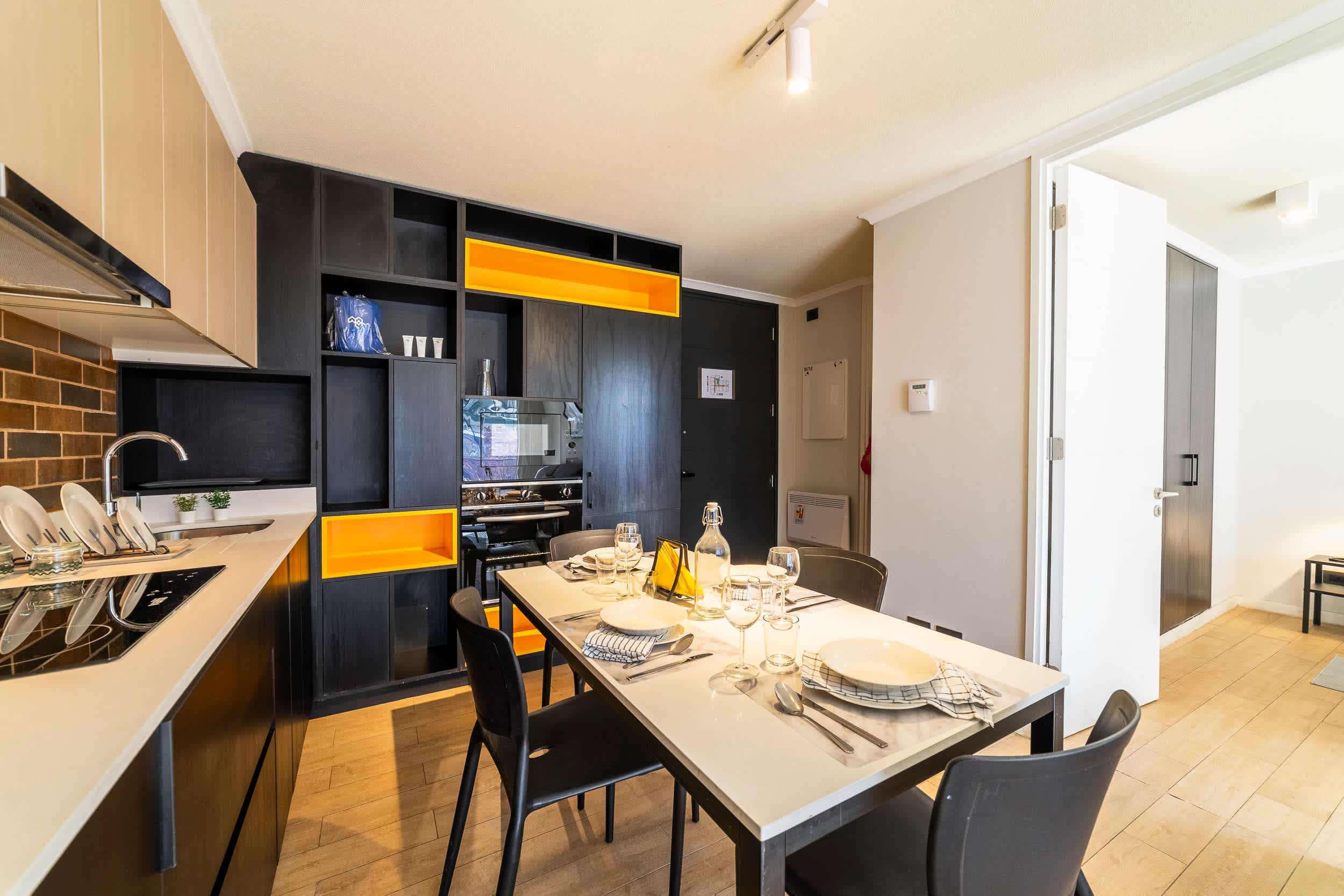 Private kitchen with bold yellow shelving, built-in appliances, and a dining table set for two.