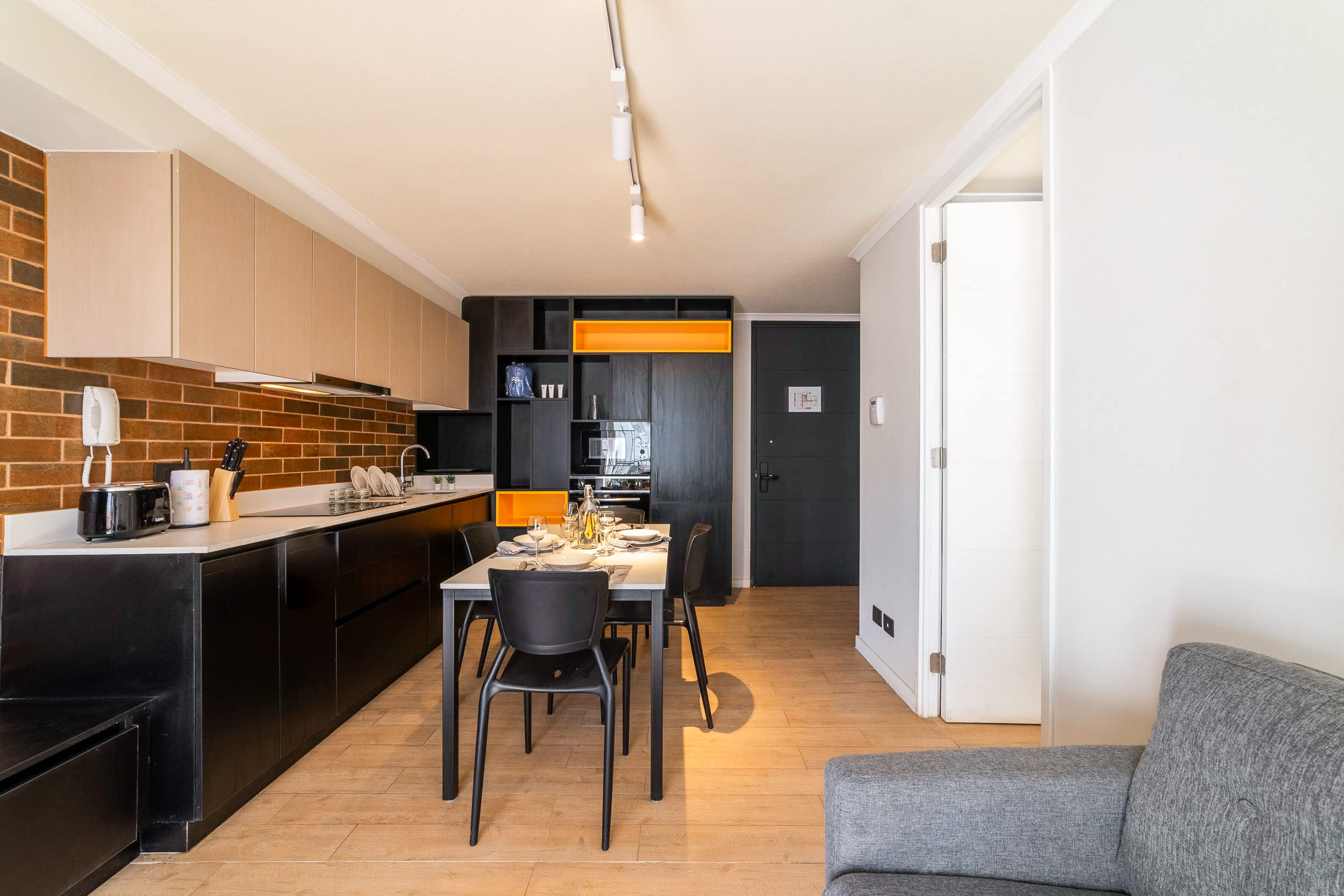 Private kitchen and dining area with a warm brick backsplash, modern black cabinetry, and a table set for shared meals.
