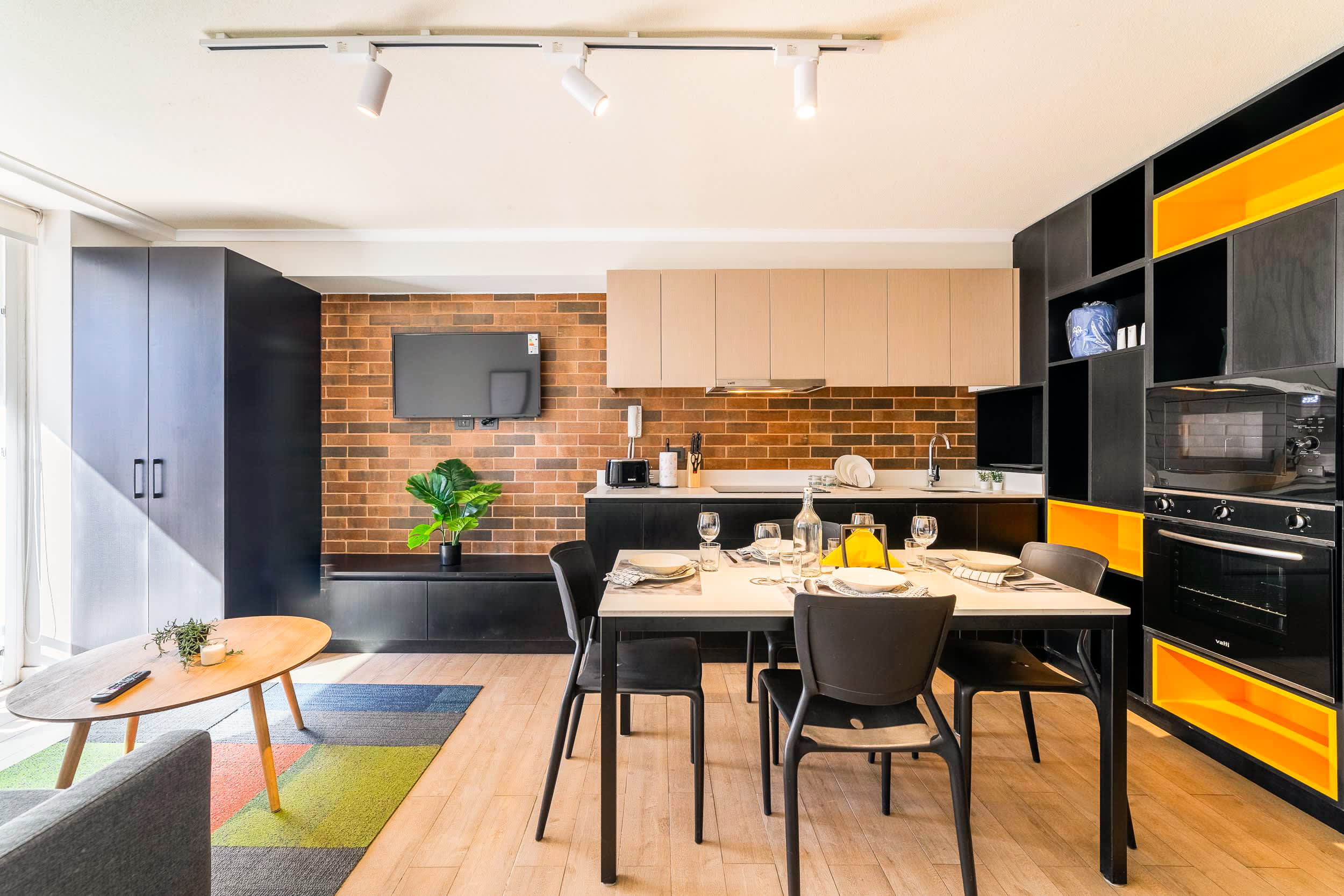 Contemporary kitchen and dining area with a brick backsplash, colorful cabinetry, integrated appliances, and a table set for relaxed meals.