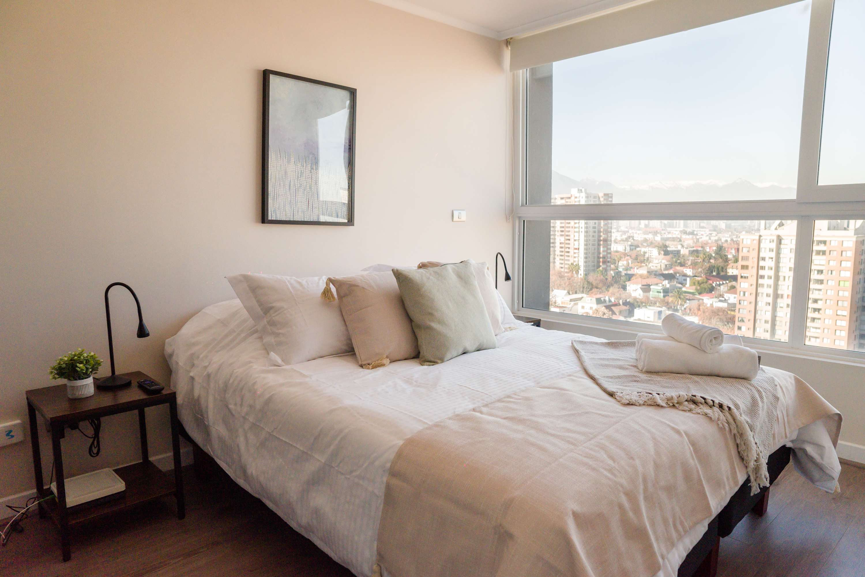 Bright bedroom with crisp white linens, reading lamps, and sweeping city-and-snowy-mountain views through the corner windows.